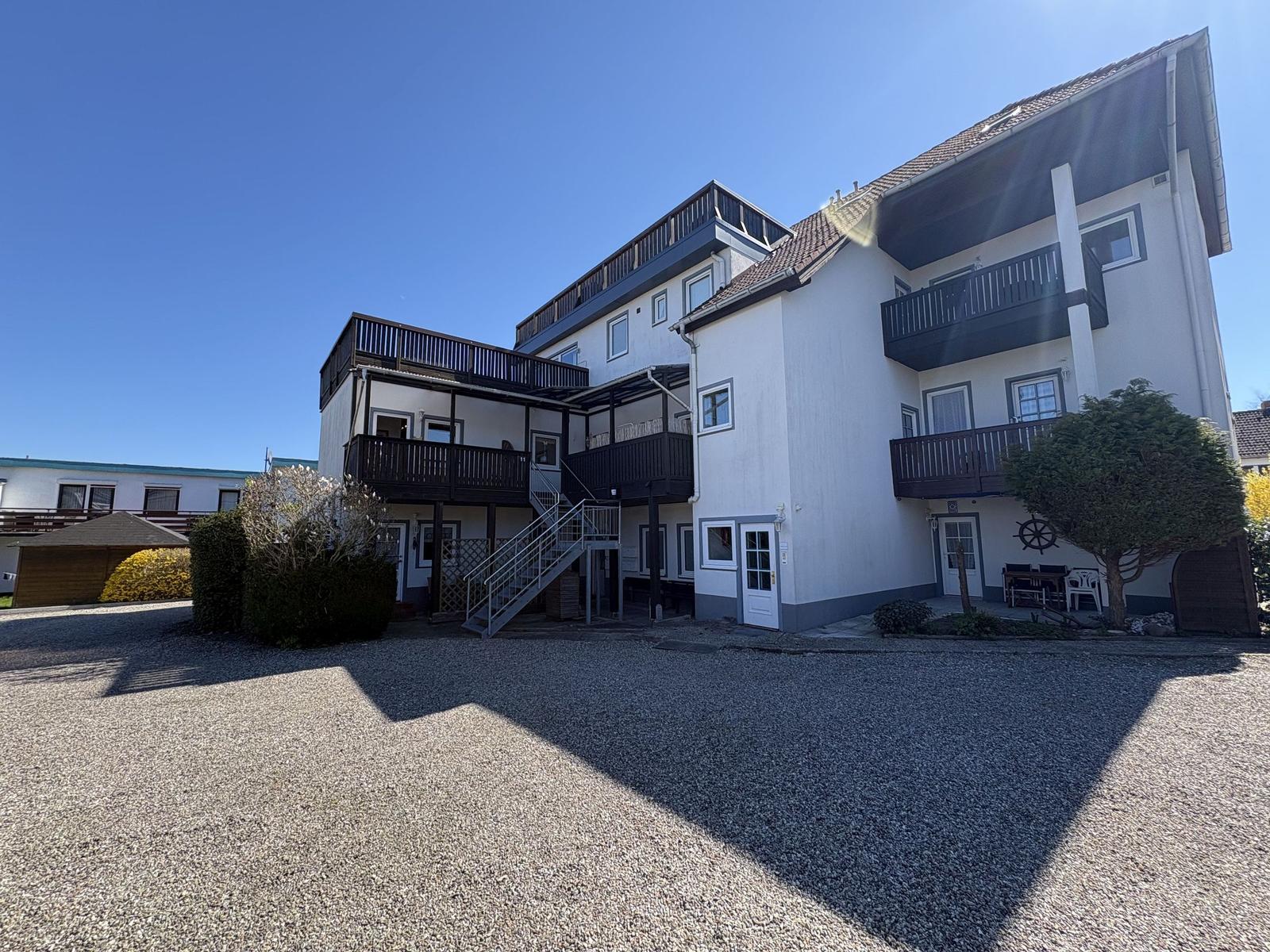 Wohnhaus mit Balkonen und Terrasse im Freien. Helle Fassade und klare Linien.