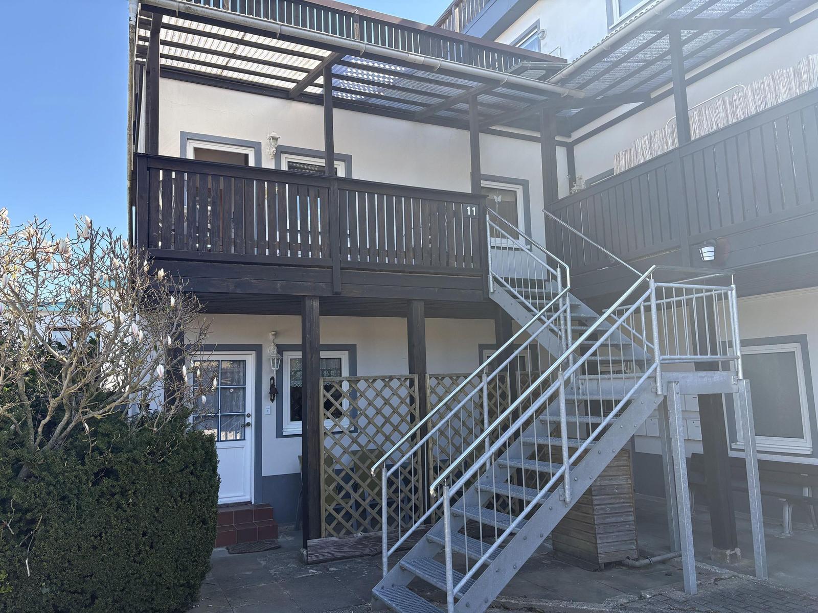 Haus mit Holzterrasse und Metalltreppe zur zweiten Etage.
