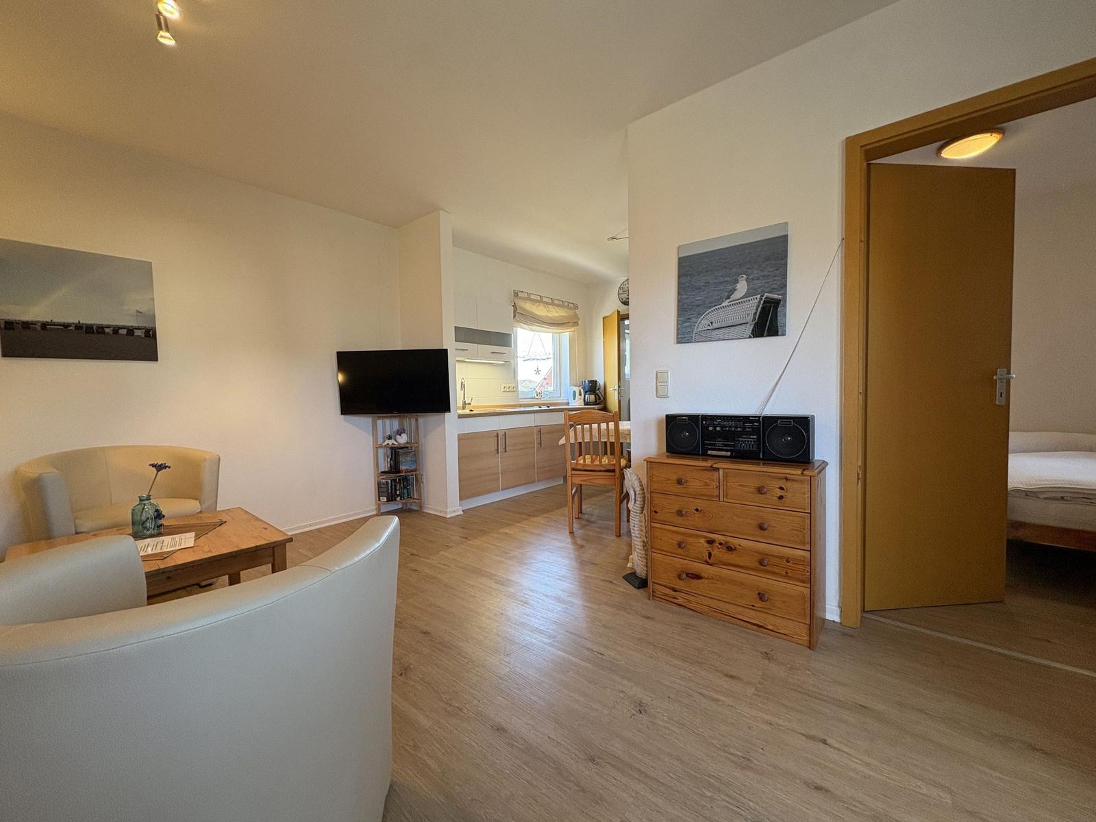 Wohnzimmer mit TV, Küche und Schlafzimmer. Holzboden und hölzerne Möbel.