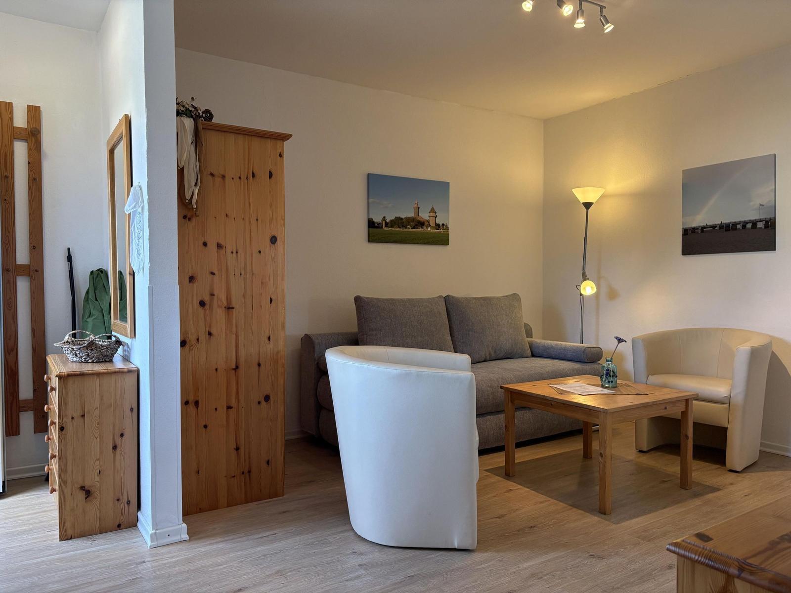 Wohnzimmer mit Sofa, zwei Sesseln, Holztisch und Wandbildern.