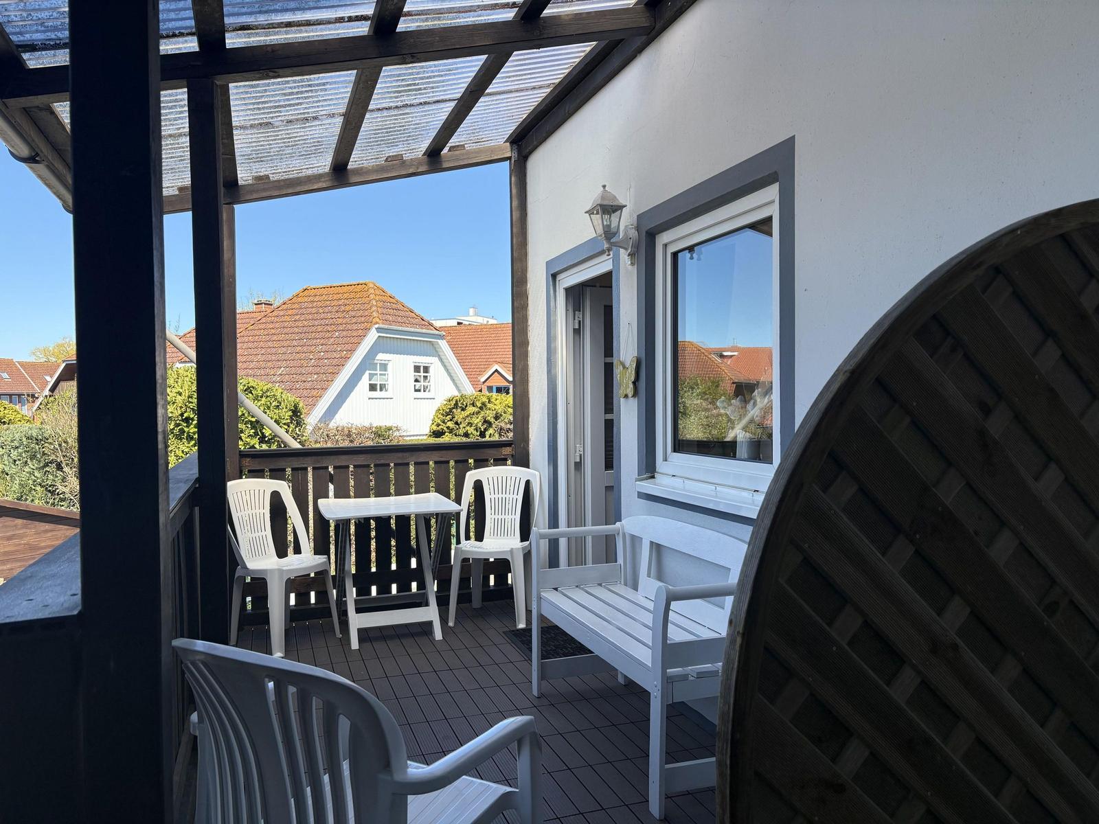 Terrasse mit Tisch, Stühlen und Bank unter Dach. Blick auf Wohnhäuser.