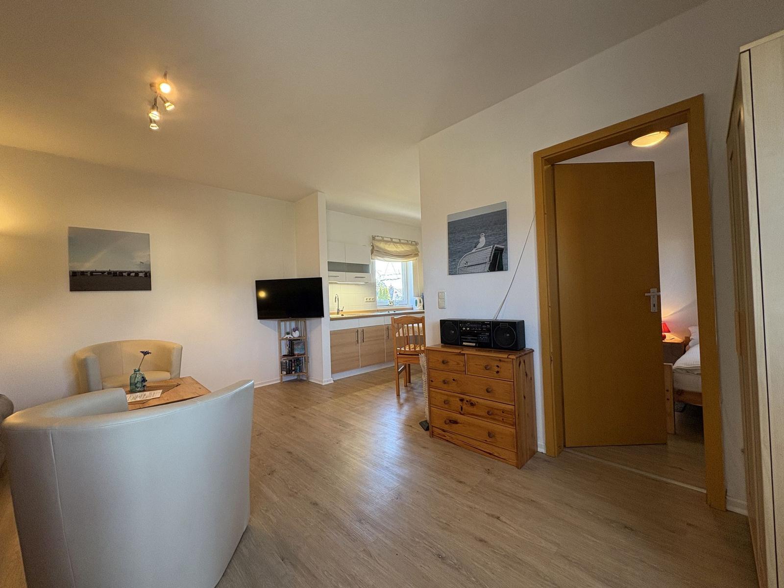 Wohnbereich mit Küchenzeile, TV und Schlafzimmer im Hintergrund.