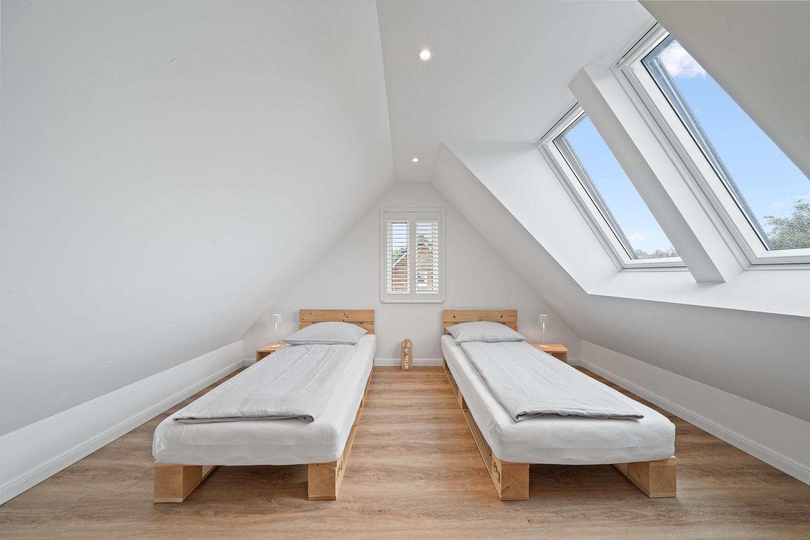 Two bedrooms with wooden beds and skylights. Wooden floor and white walls.
