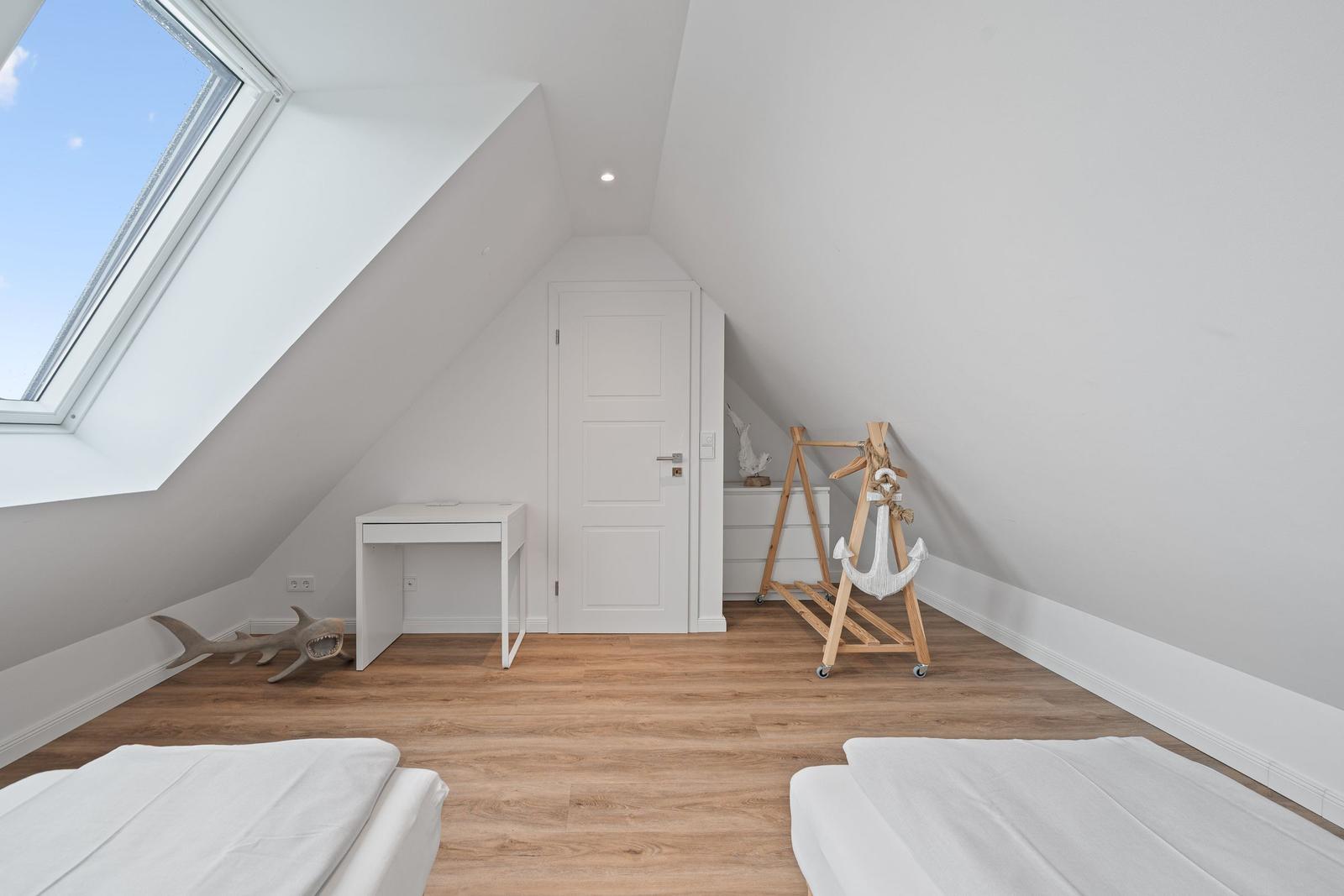 Room with sloped ceiling, skylight, two beds, desk, and wooden anchor stand.