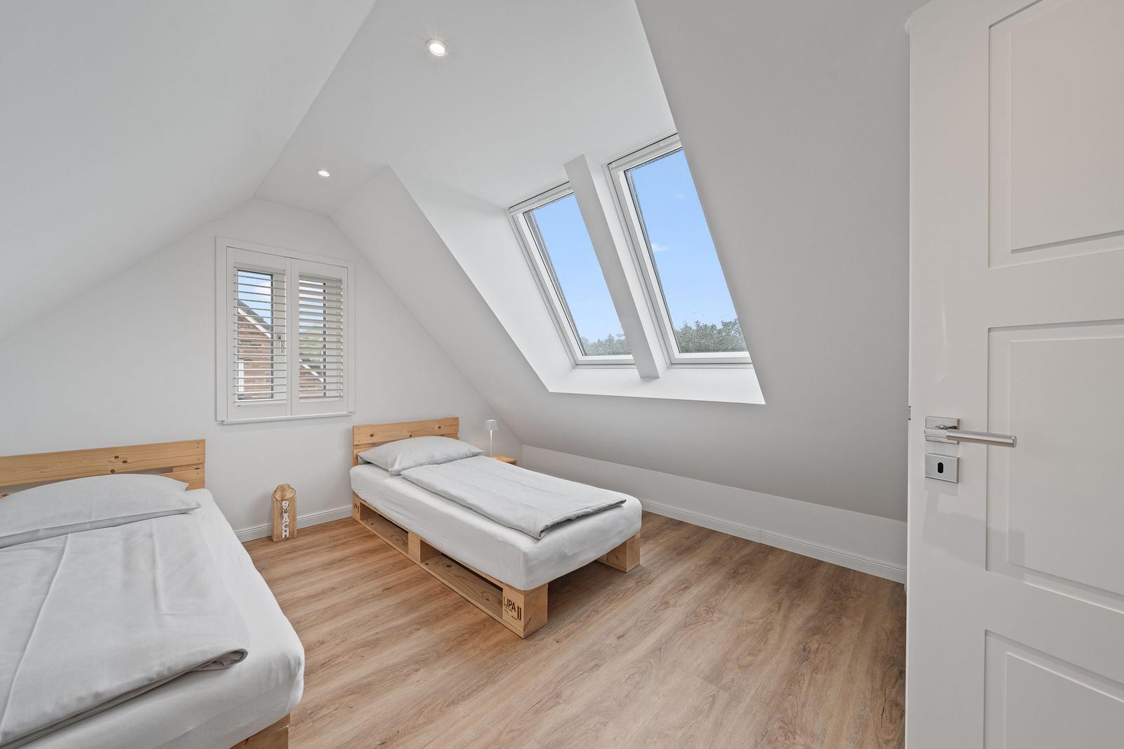 Room with two beds, skylight, and wooden floor.