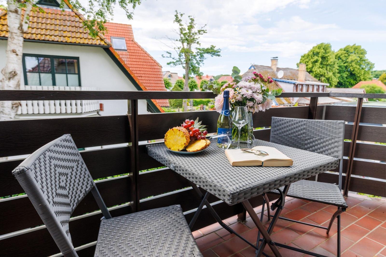 Terrasse mit Tisch, Stühlen, Obst und Blumen. Blick auf Dächer und Bäume.