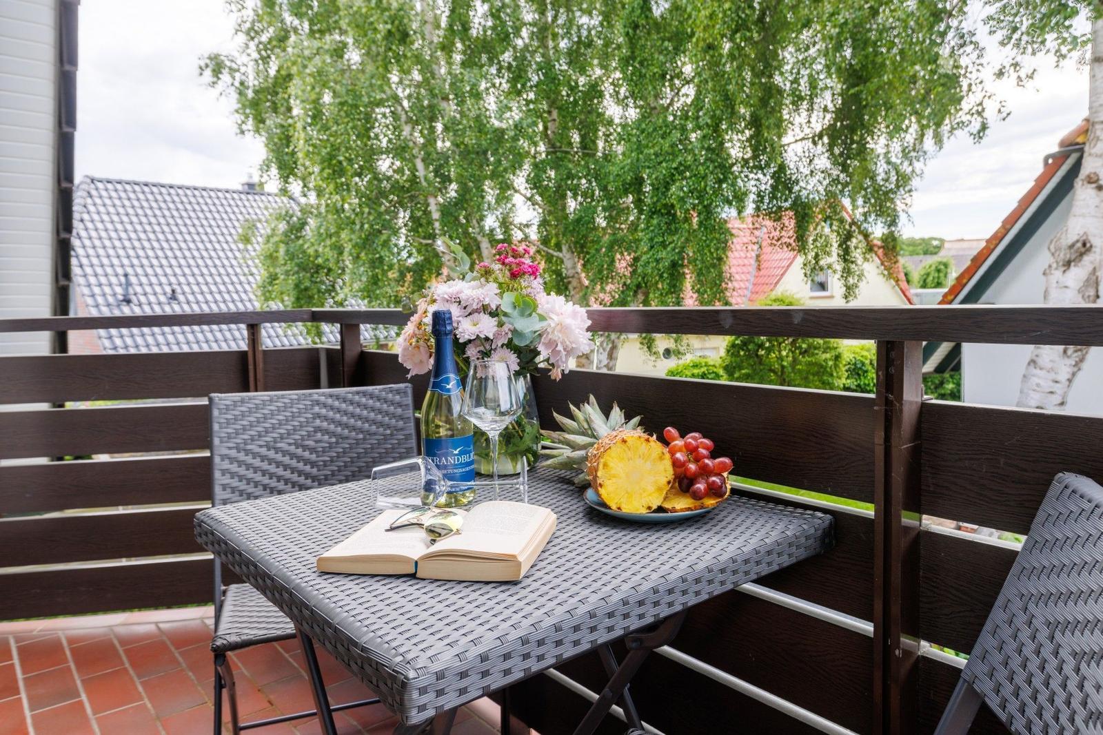 Terrasse mit Tisch, Stühlen, Blumen, Obst und Weinflasche.