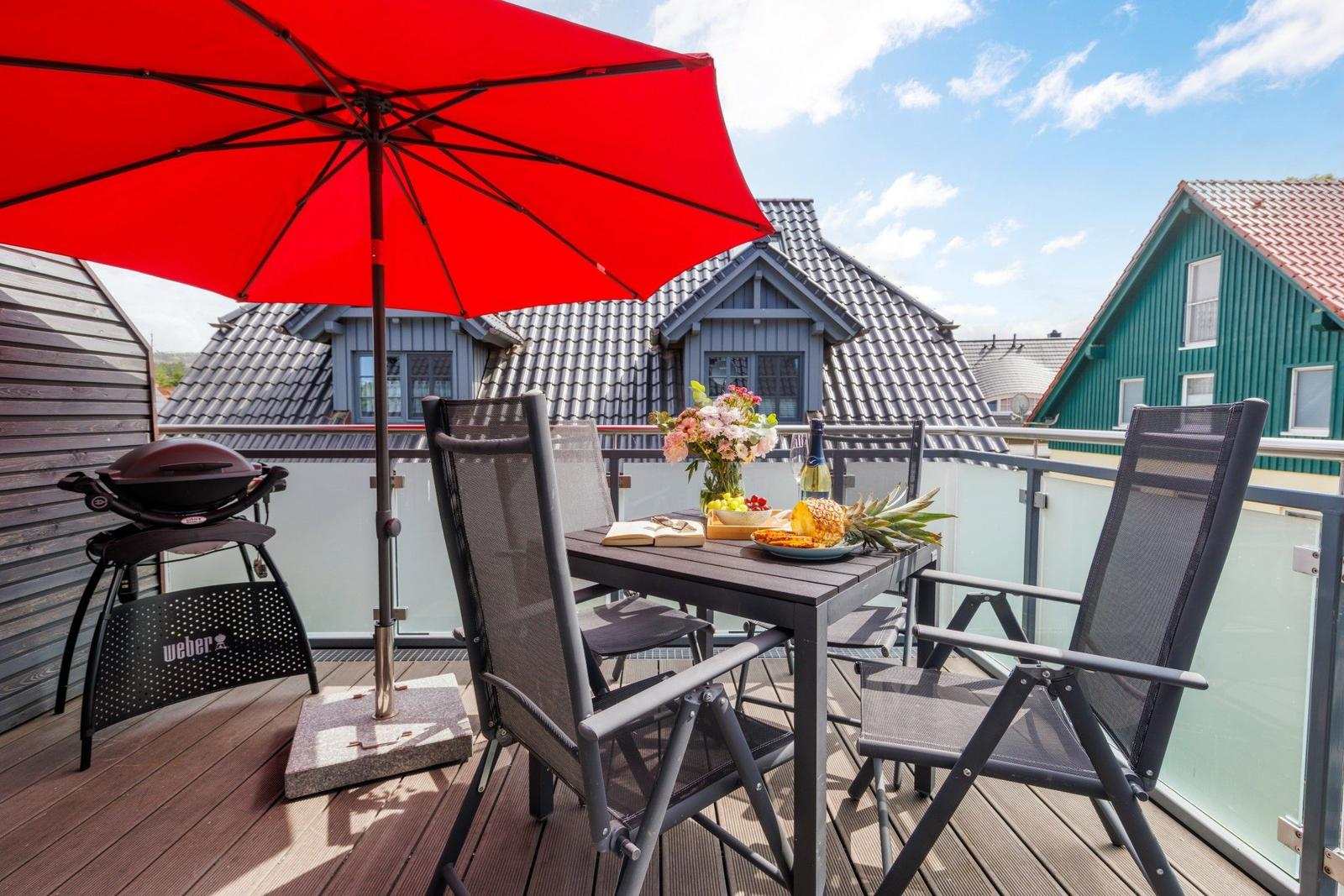 Terrasse mit Tisch, Stühlen, Sonnenschirm und Grill. Blick auf Dächer und Häuser.