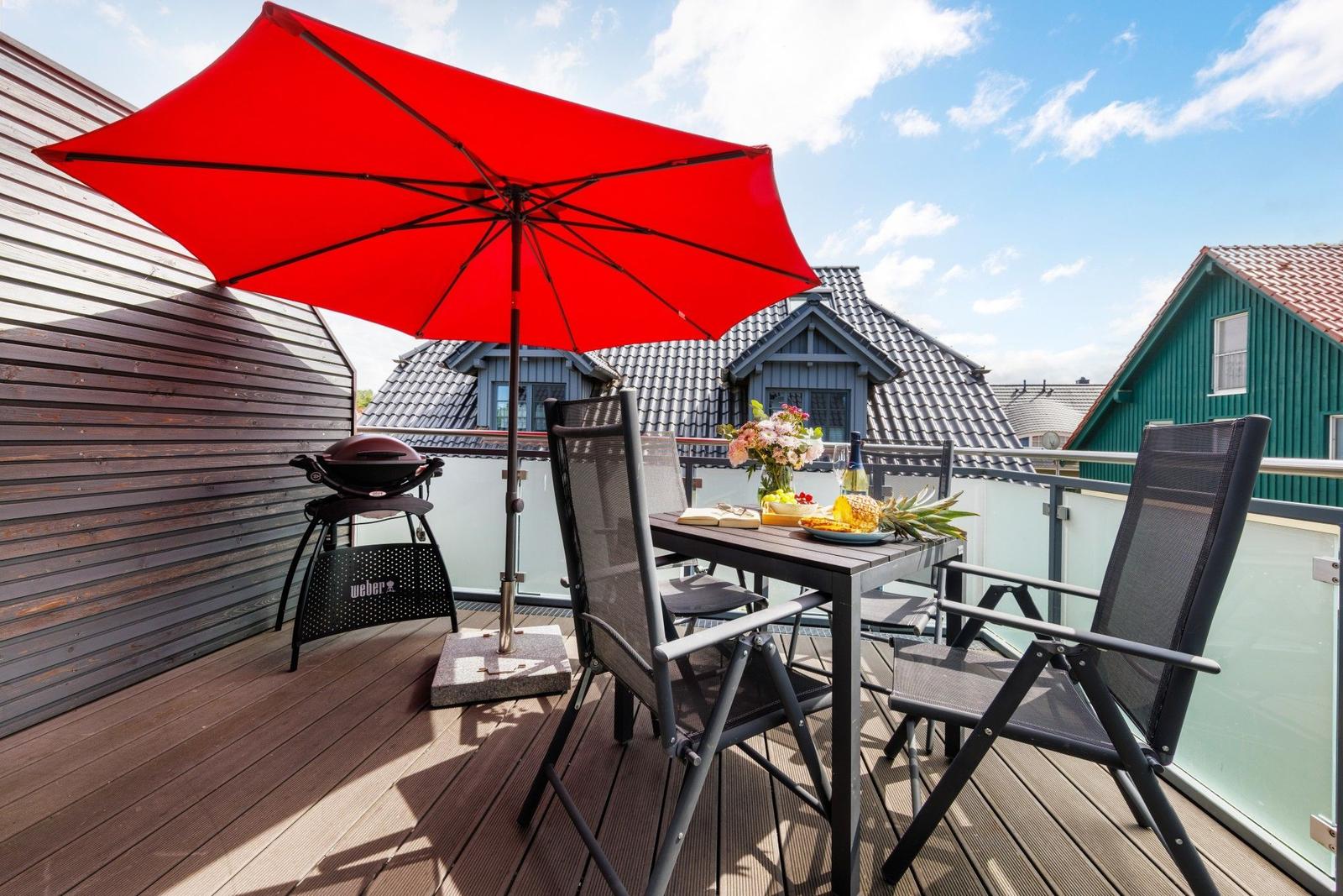 Terrasse mit Tisch, Stühlen, rotem Sonnenschirm und Grill.