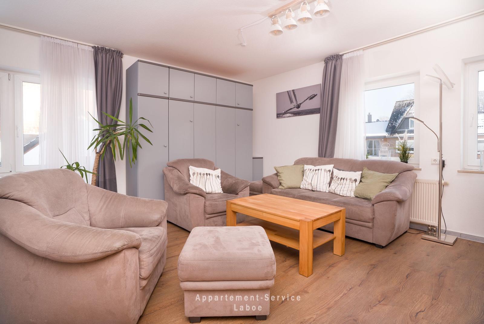 Wohnzimmer mit Sofa, Sesseln und Holztisch. Hintergrund: Kleiderregal und Fenster.