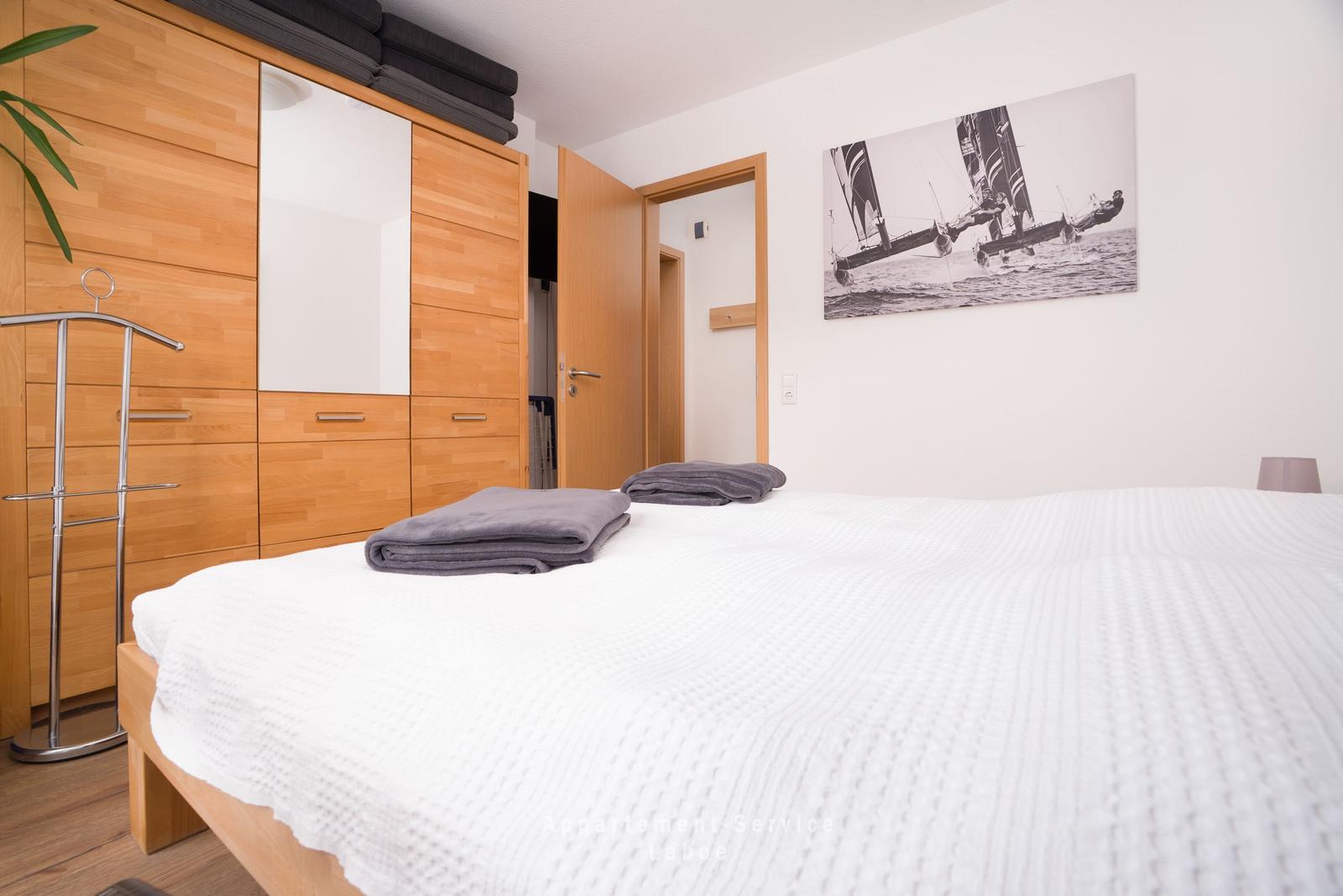 Schlafzimmer mit Bett, Holzschrank und Segelboot-Bild an der Wand.