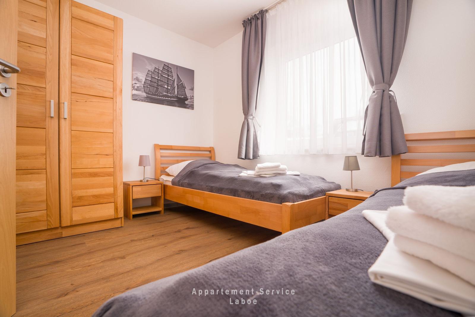 Zimmer mit zwei Betten, Holzmöbel und Fenster mit Vorhängen.