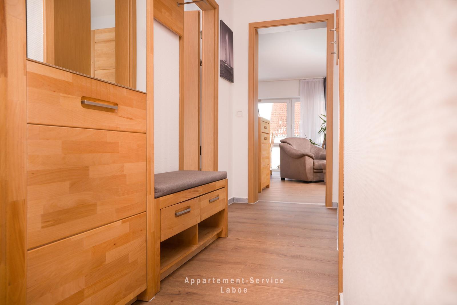 Flur mit Holzmöbeln und Blick in Wohnzimmer mit Sessel.