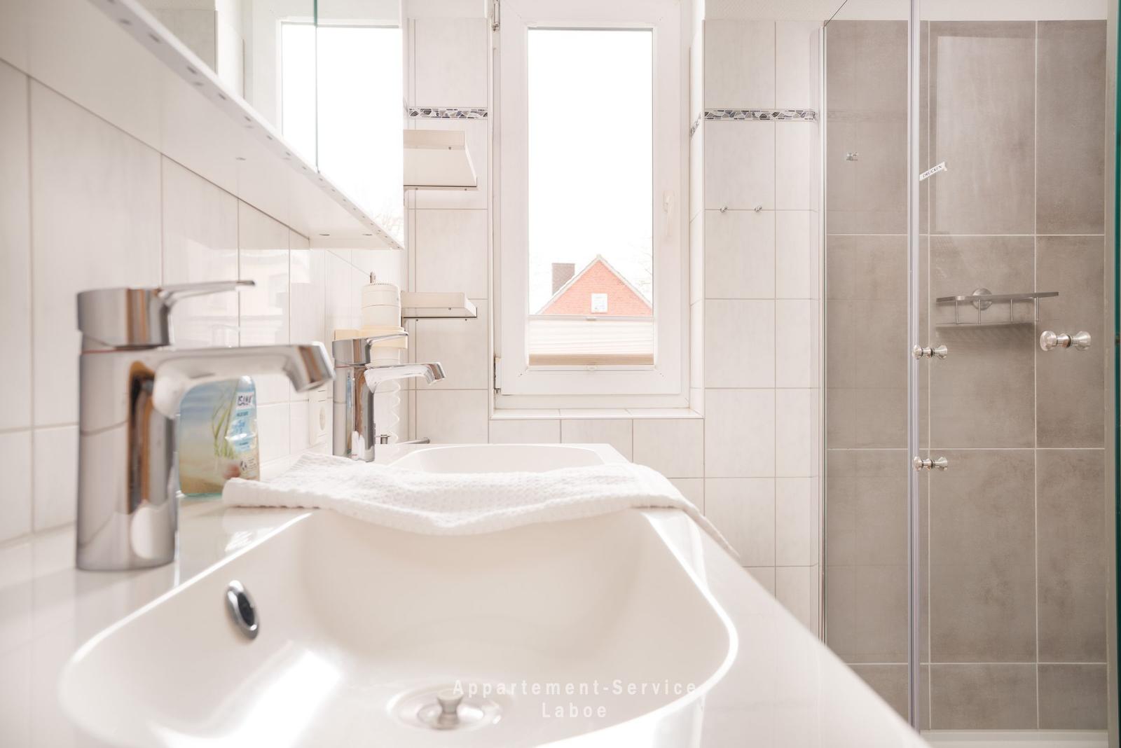 Badezimmer mit Dusche, Waschbecken und Fenster mit Blick auf Dach.