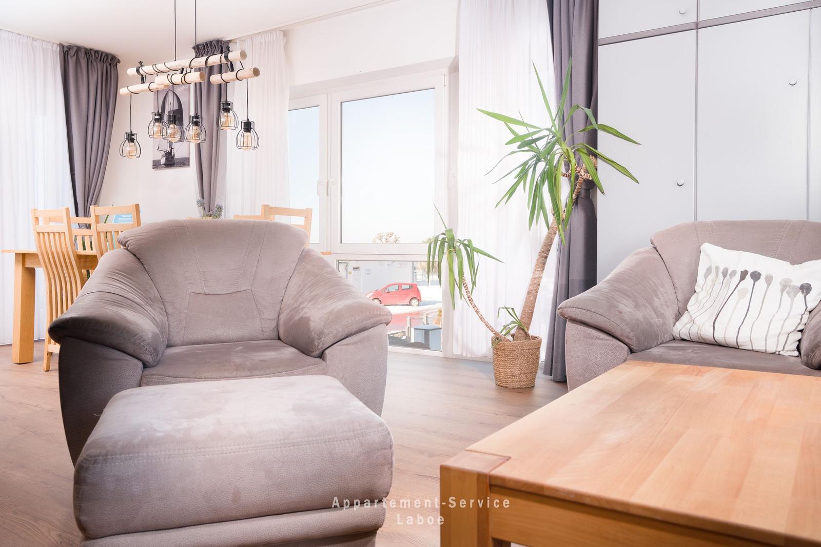 Wohnzimmer mit Sofa, Sessel und Esstisch. Fensterblick auf Straße mit Auto.