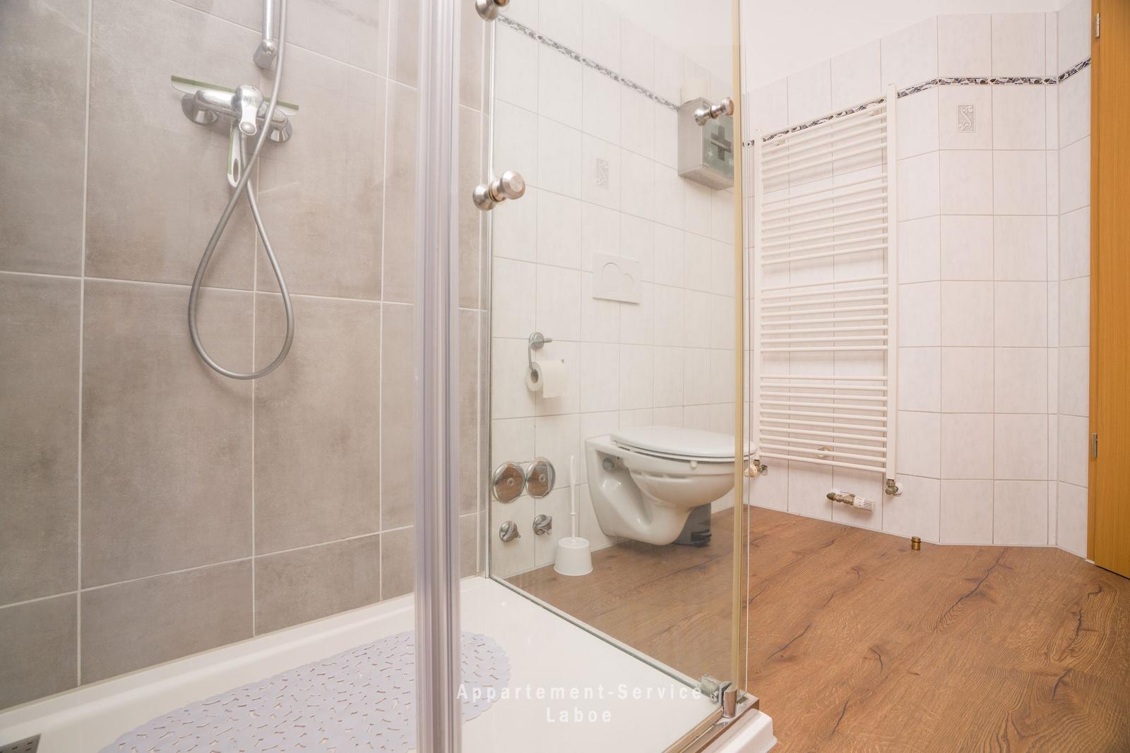 Bad mit Dusche, Toilette und Heizkörper an der Wand.