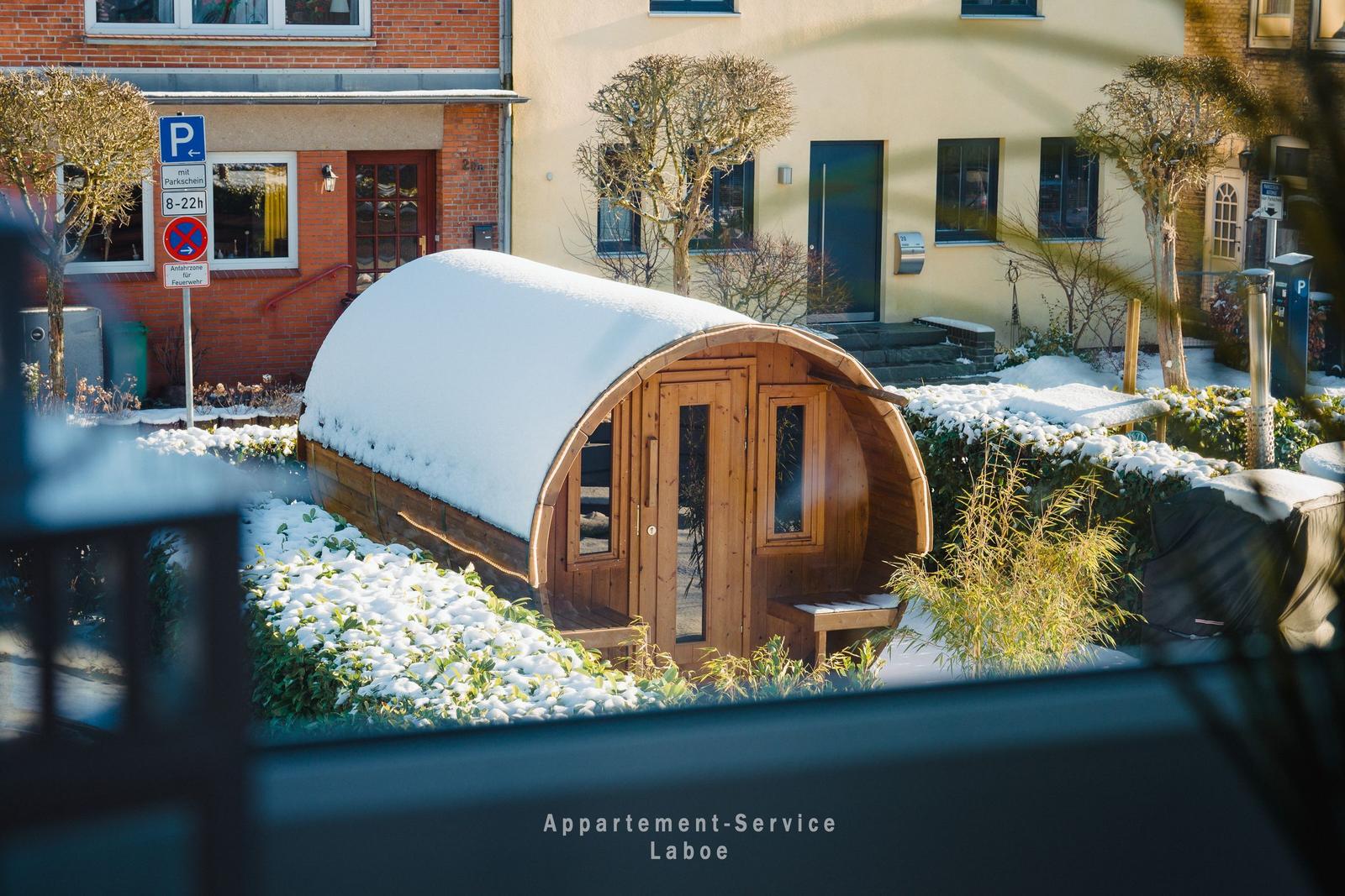 Holzschlauchhaus mit Schneebedeckter Dachkrümmung im Garten vor Wohnhäusern
