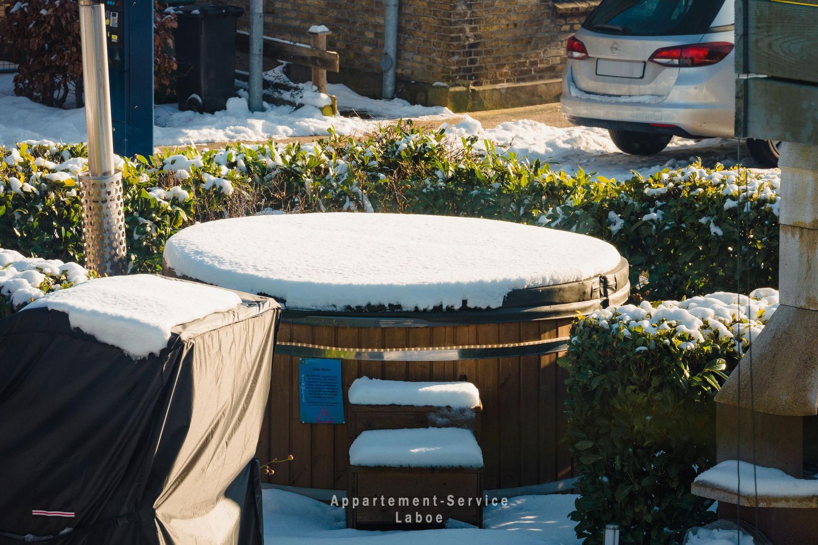 Schnee bedeckt Whirlpool und Gartenmöbel im Außenbereich.