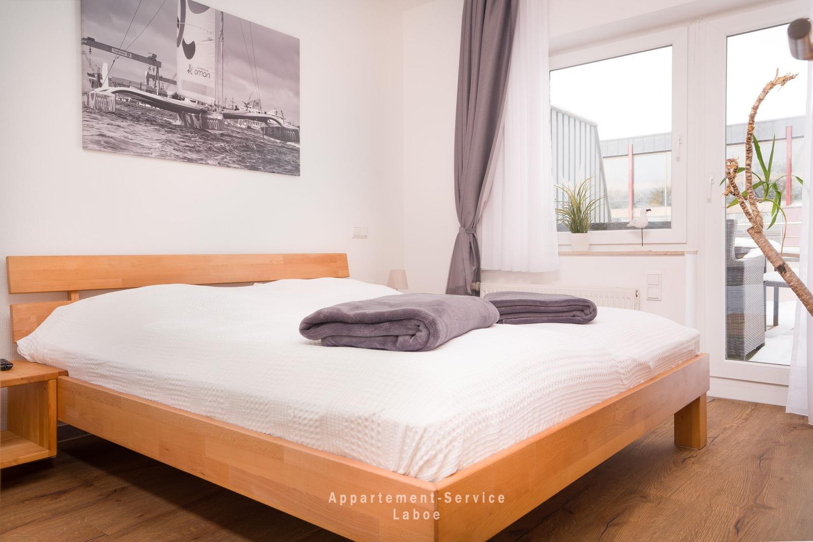 Ein Schlafzimmer mit Holzbett, Fenster und Blick auf Balkon.