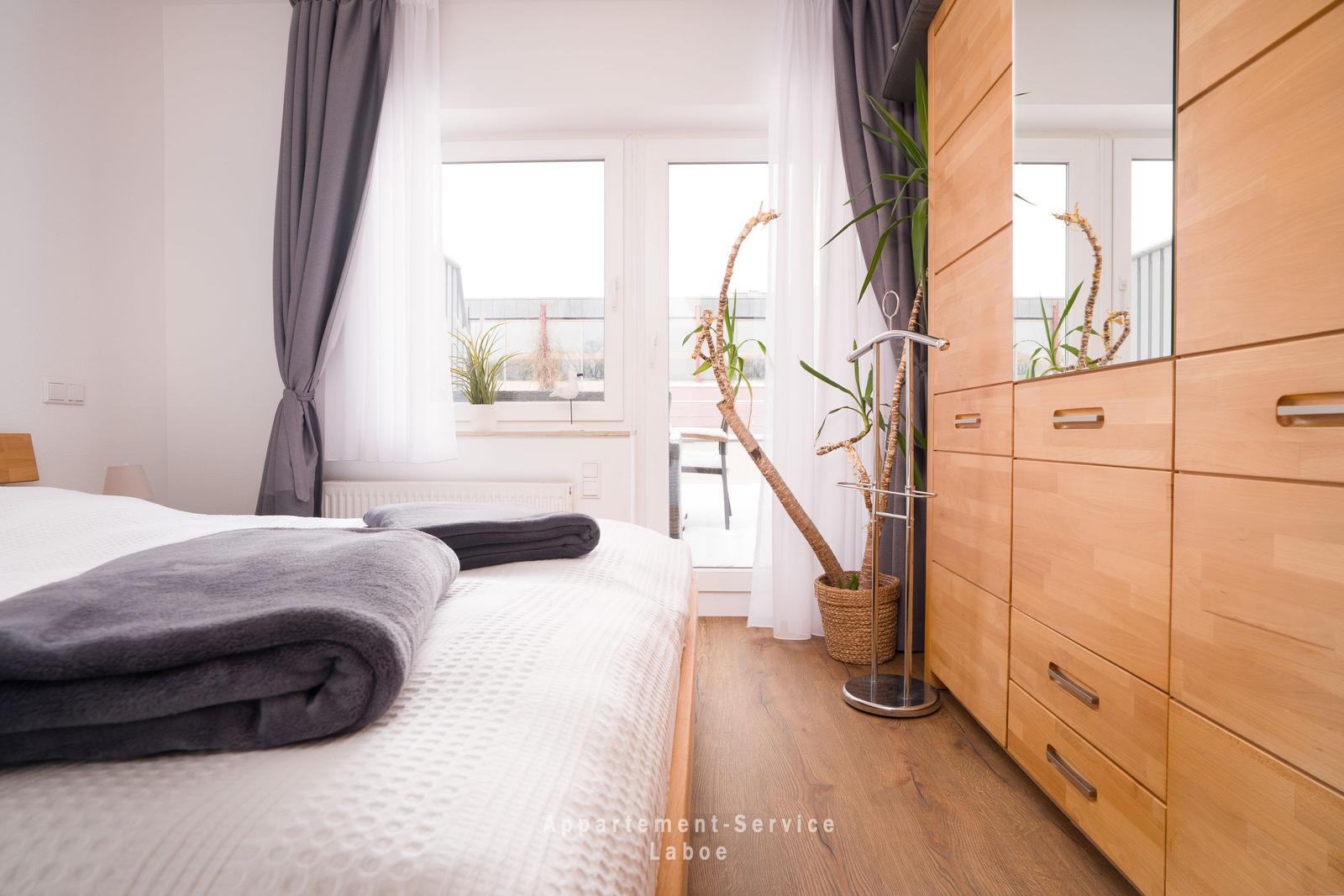 Schlafzimmer mit Bett, Kleiderschrank und Fenster zur Terrasse.
