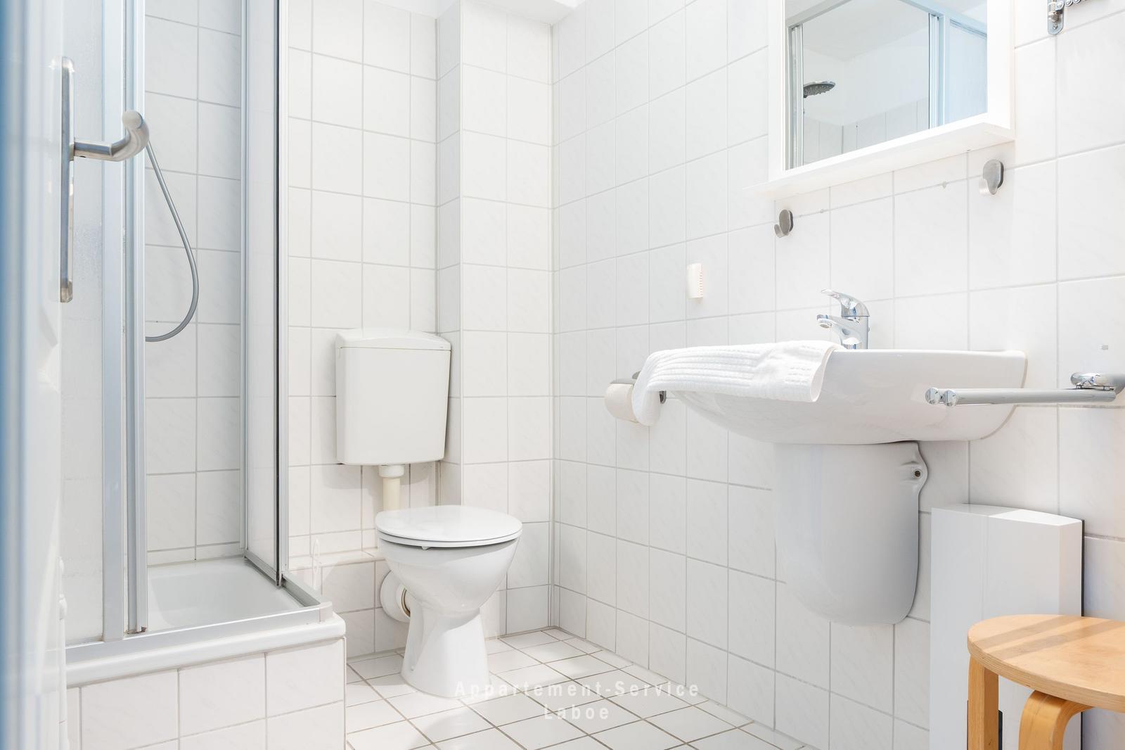 Badezimmer mit Dusche, Toilette und Waschbecken. Weiße Fliesen und Spiegel.