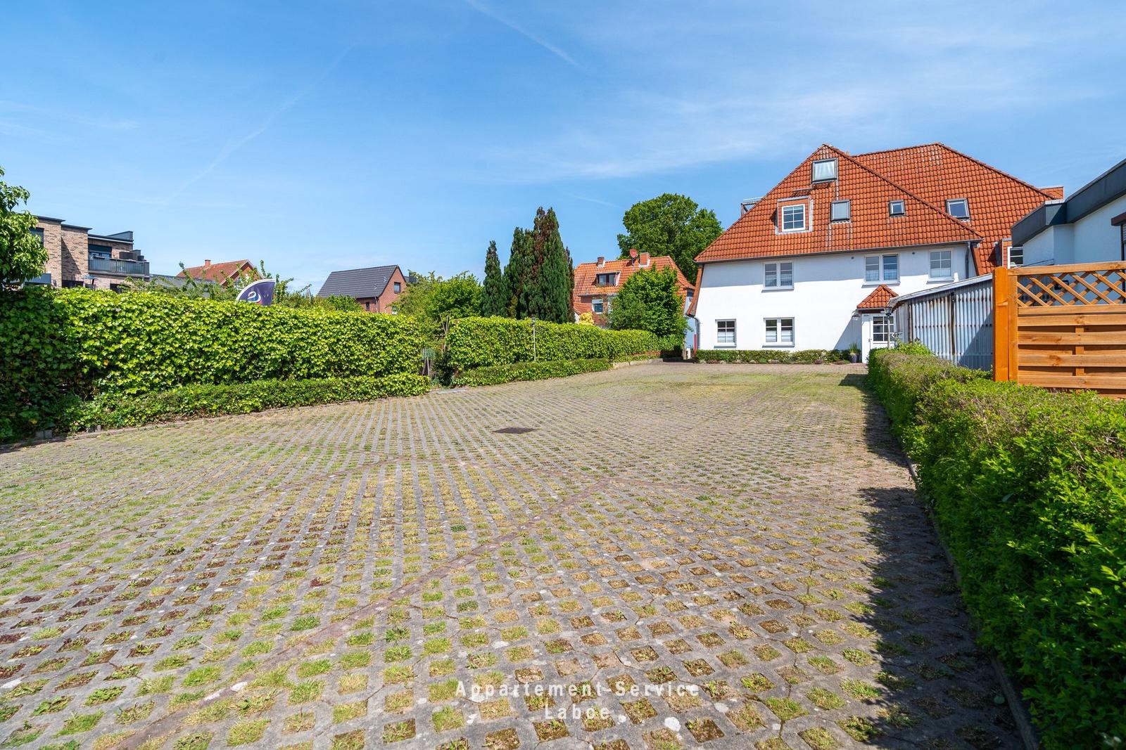 Gartenweg mit Pflastersteinen führt zu einer weißen Villa mit rotem Dach.