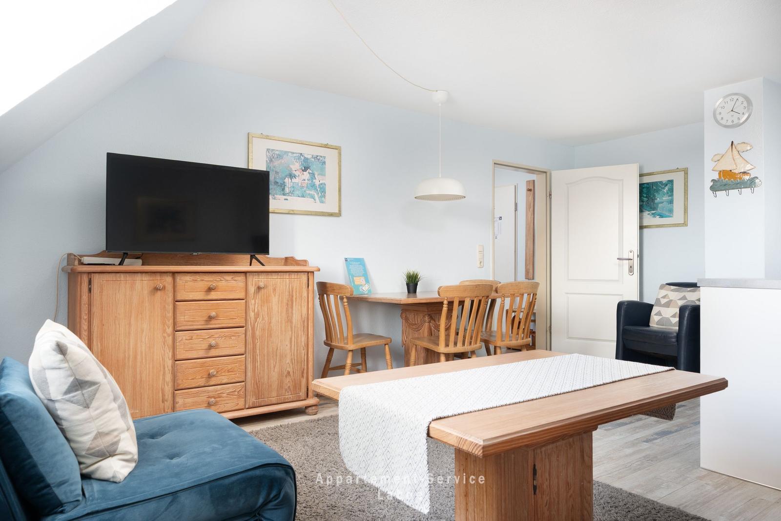 Wohn- und Essbereich mit Holzmöbeln, Fernseher und Tisch. Decke mit Dachneigung.