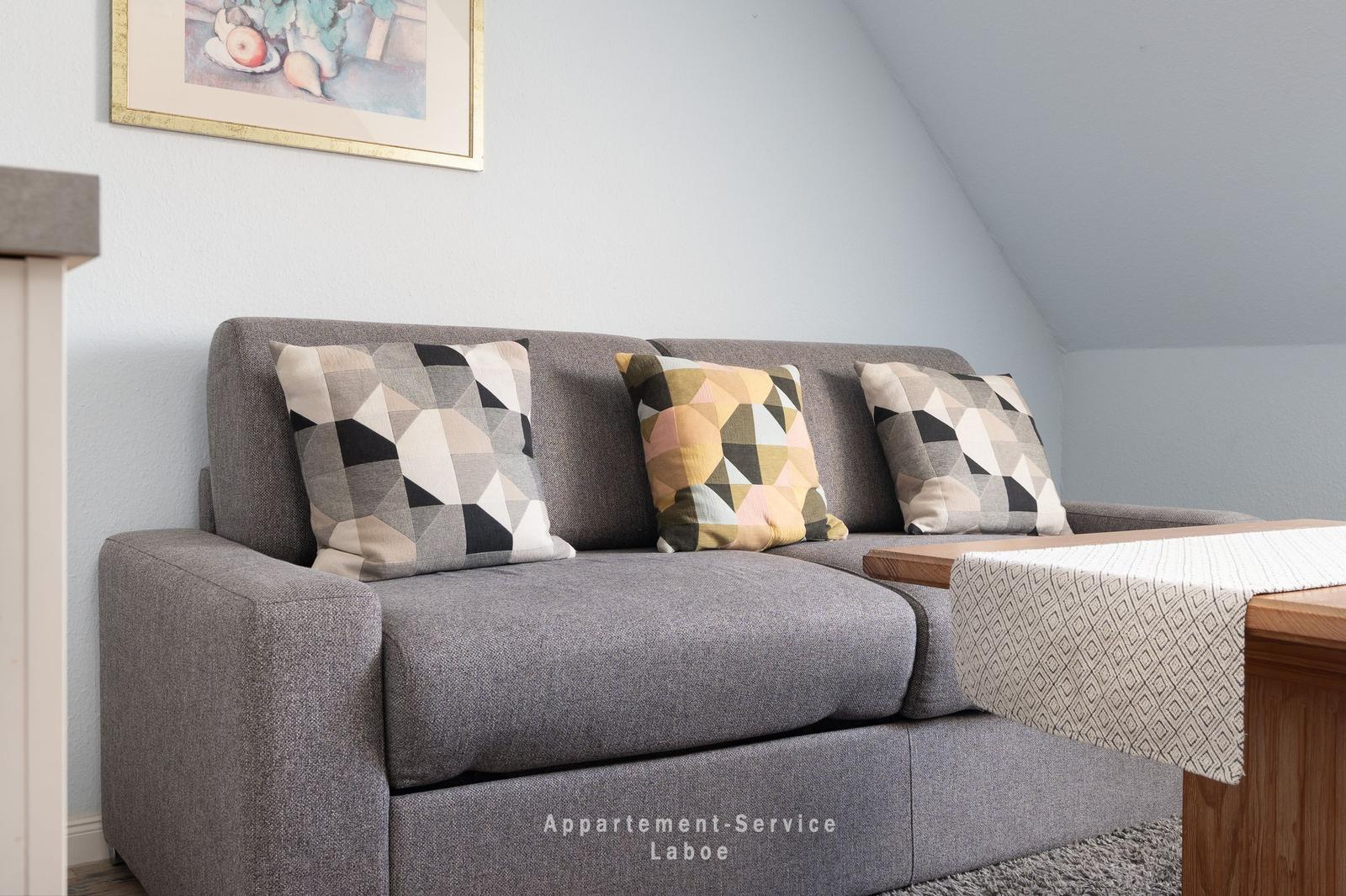 Grauer Sofa mit drei Kissen und Holztisch im Wohnzimmer mit schräger Decke.