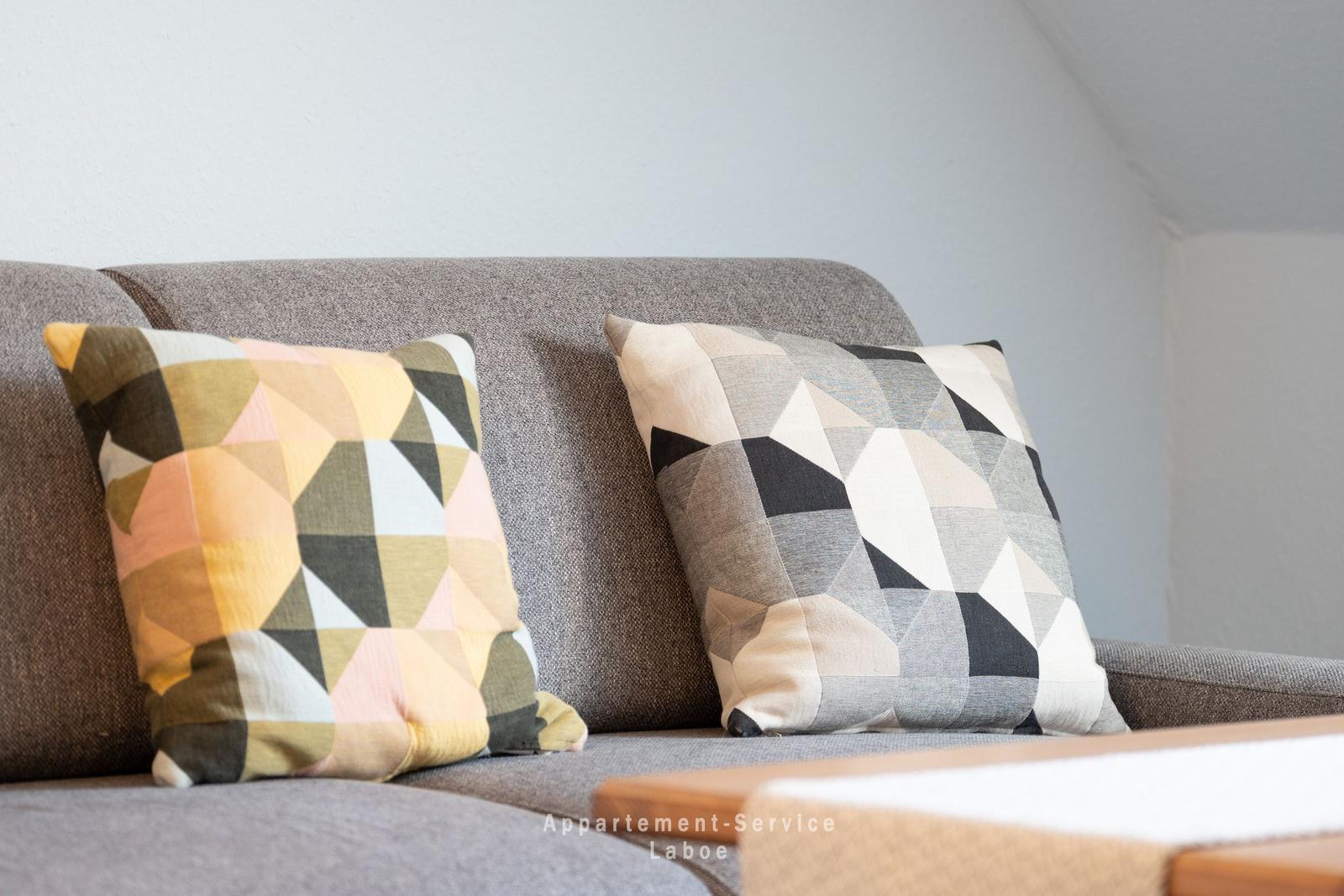 Zwei Kissen mit geometrischen Mustern auf einem grauen Sofa.