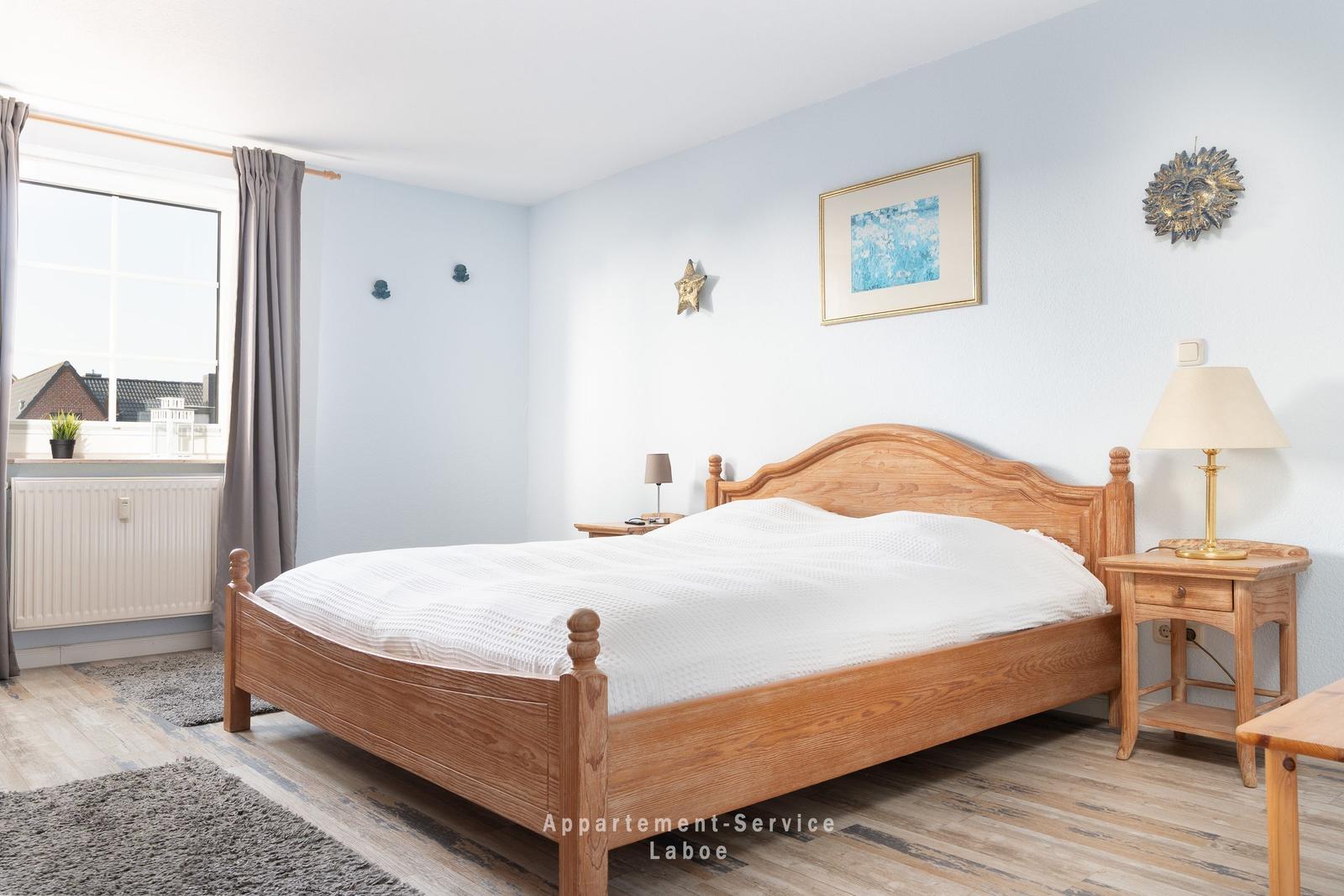 Ein Schlafzimmer mit Holzbett, Nachttisch und Fenster mit Vorhängen.
