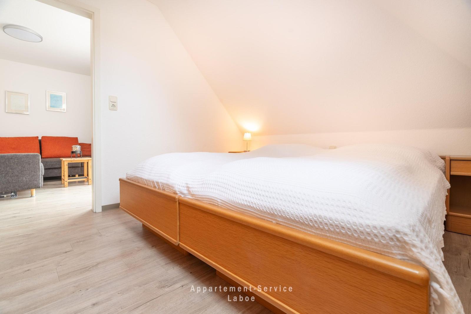 Schlafzimmer mit Doppelbett und angrenzendem Wohnbereich mit Sofa.