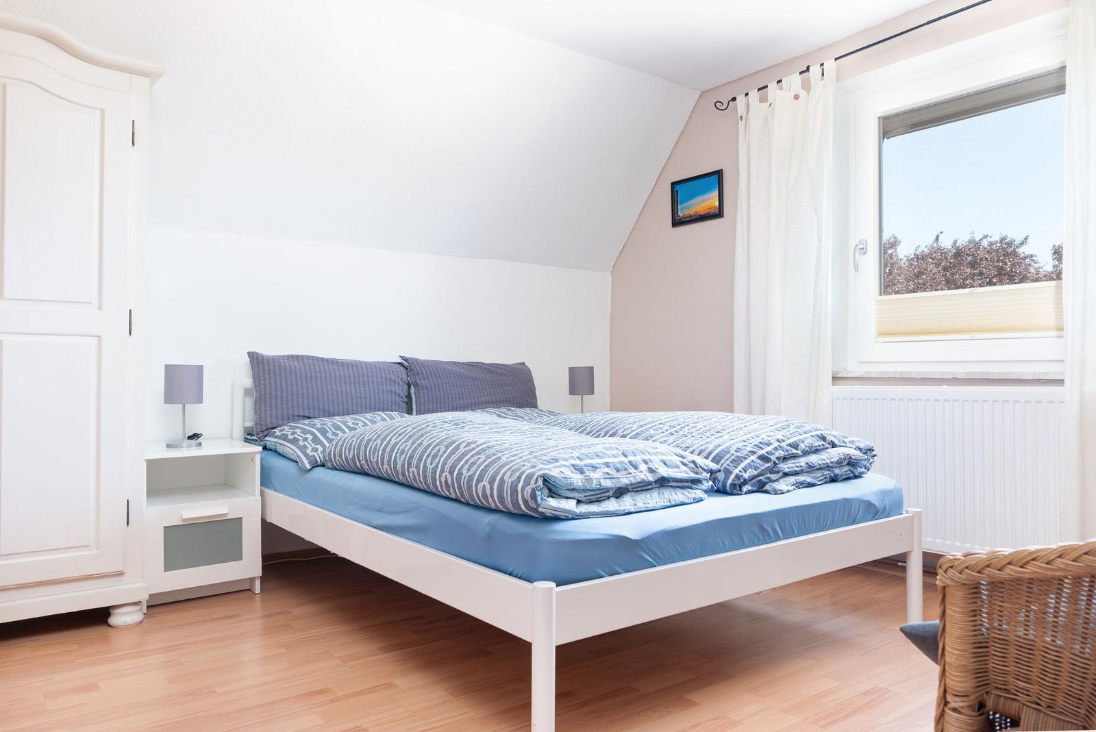 Schlafzimmer mit Doppelbett, weißen Möbeln und Fenster mit Blick nach draußen.