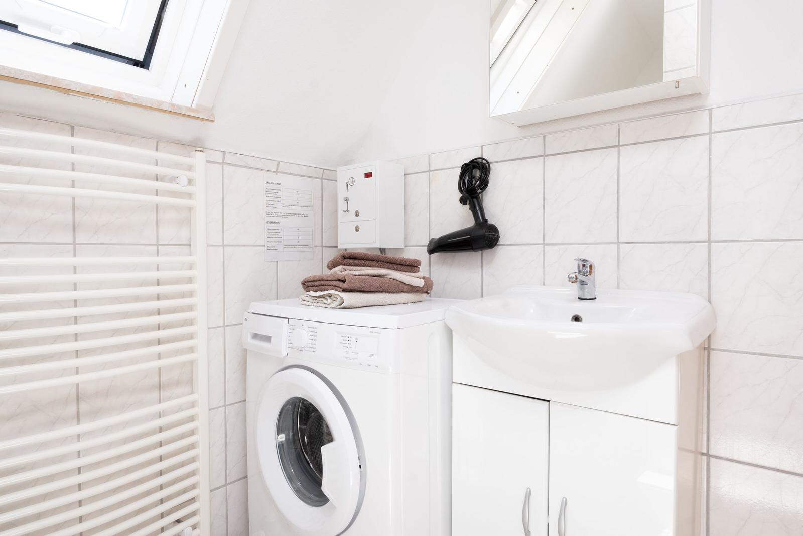 Badezimmer mit Waschmaschine, Waschbecken und Handtuchhalter.