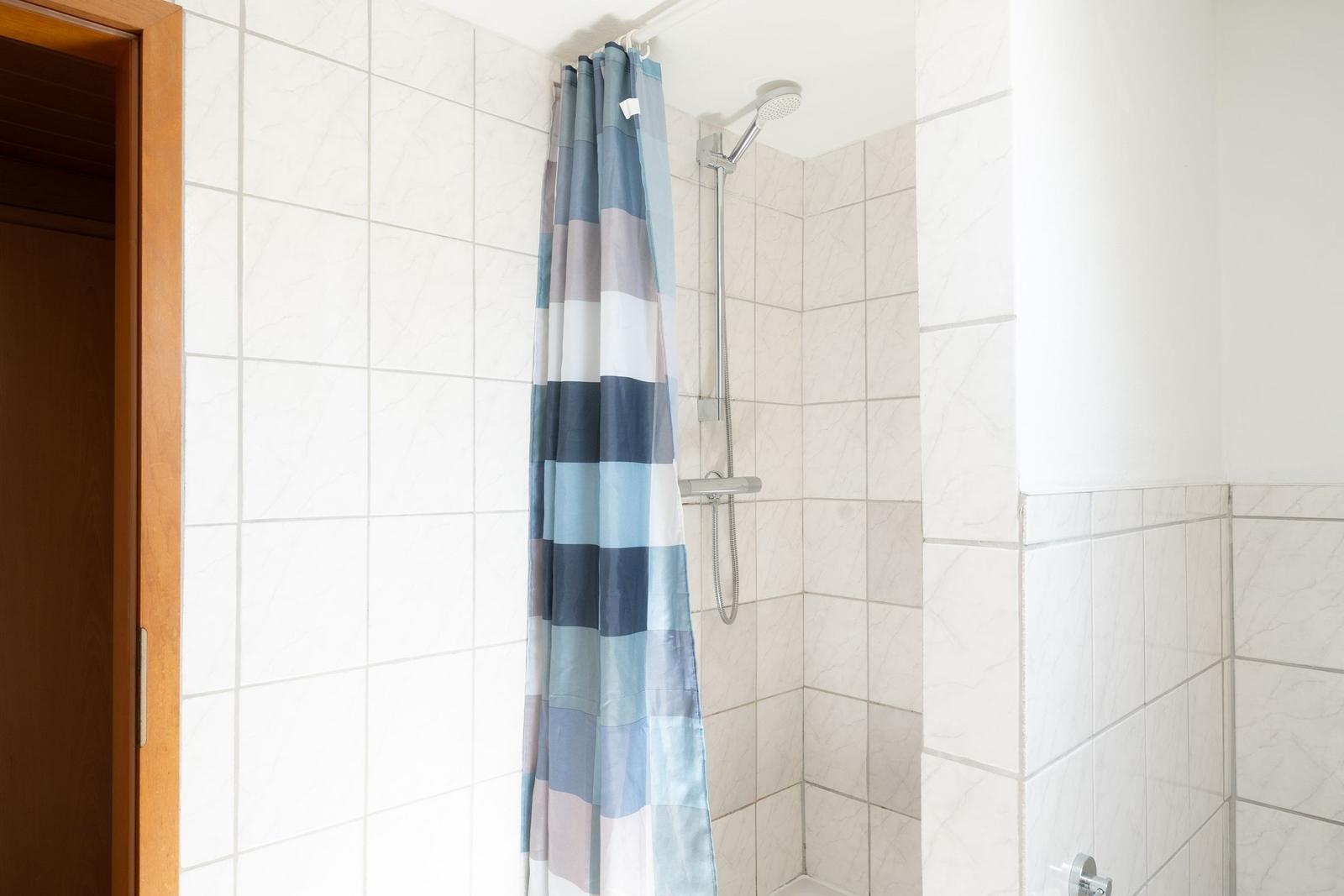 Dusche mit Duschvorhang und Handbrause in einem Badezimmer mit Fliesen.