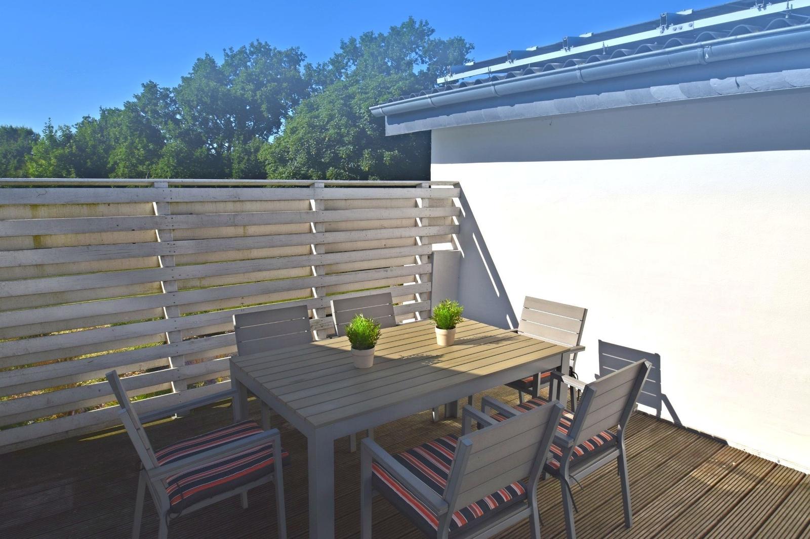 Terrasse mit Tisch und Stühlen, Holzgeländer und Blick auf Bäume.