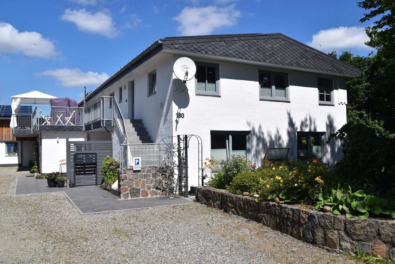 Ein zweistöckiges Haus mit Balkon, Garten und Steinmauer. Hausnummer 180.