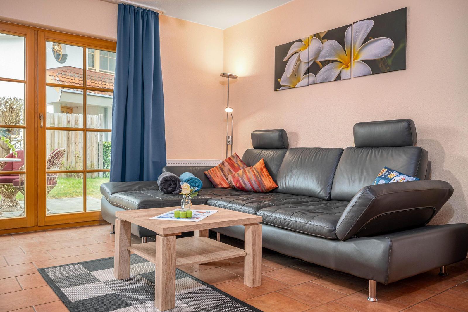 Ein Wohnzimmer mit einem grauen Sofa, einem Holztisch und einer Glastür zum Garten.