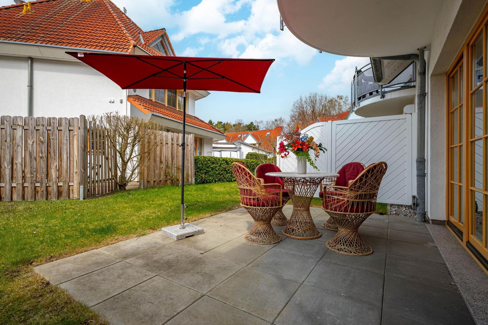 Terrasse mit rotem Sonnenschirm und Rattanmöbeln. Hinterhof mit Holzzaun und Grünfläche.