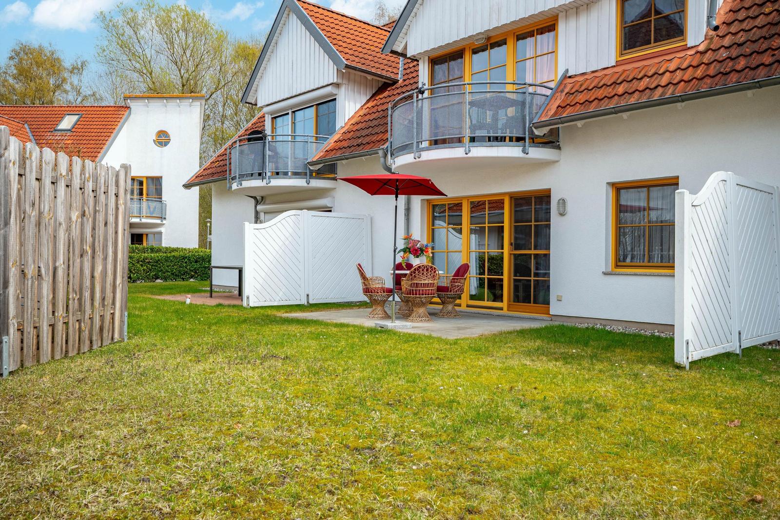 Wohnhaus mit Terrasse, rotem Sonnenschirm und Gartenbereich mit Stühlen.