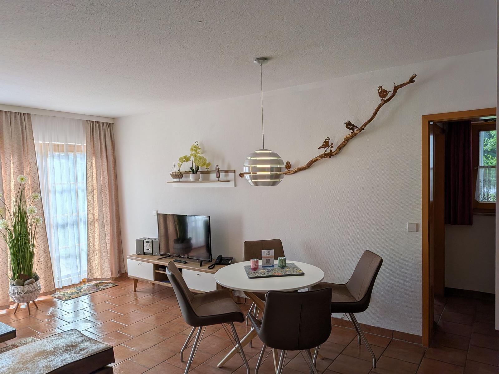 Wohn- und Essbereich mit Tisch, Stühlen, Fernseher und Wanddekoration.
