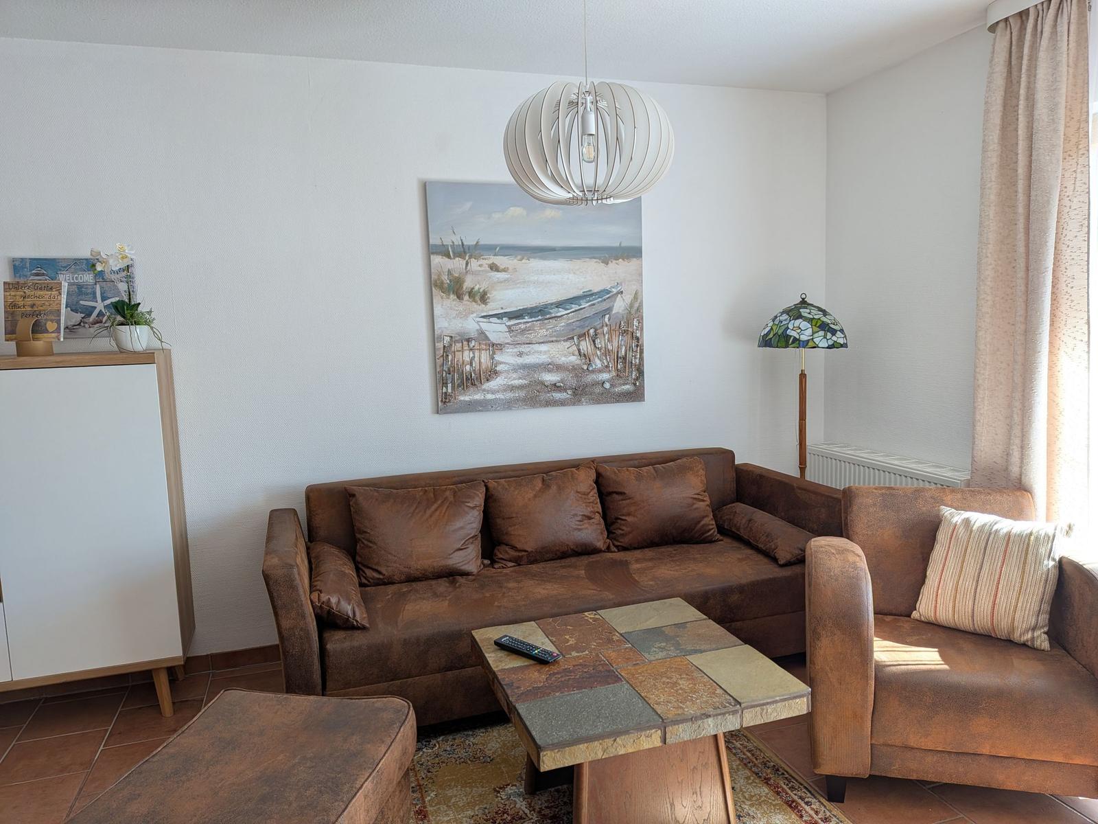 Ein Wohnzimmer mit braunem Sofa, Tisch und Wandbild.