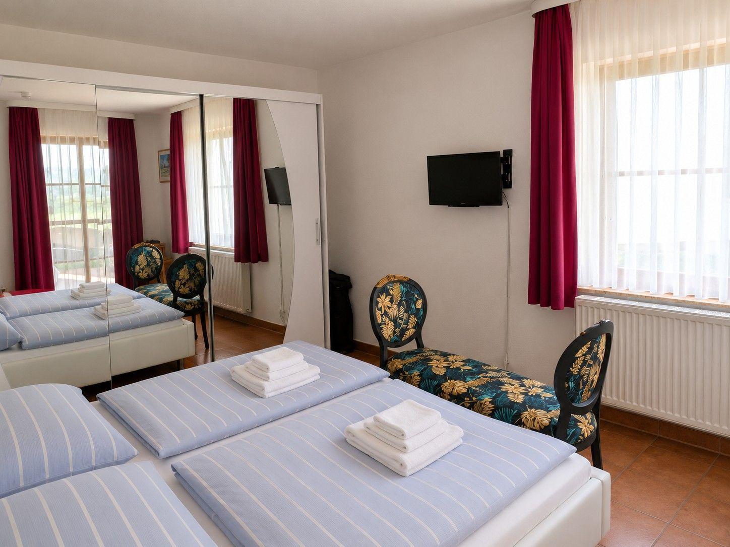 Zimmer mit Doppelbett, TV und Fenster mit roten Vorhängen.