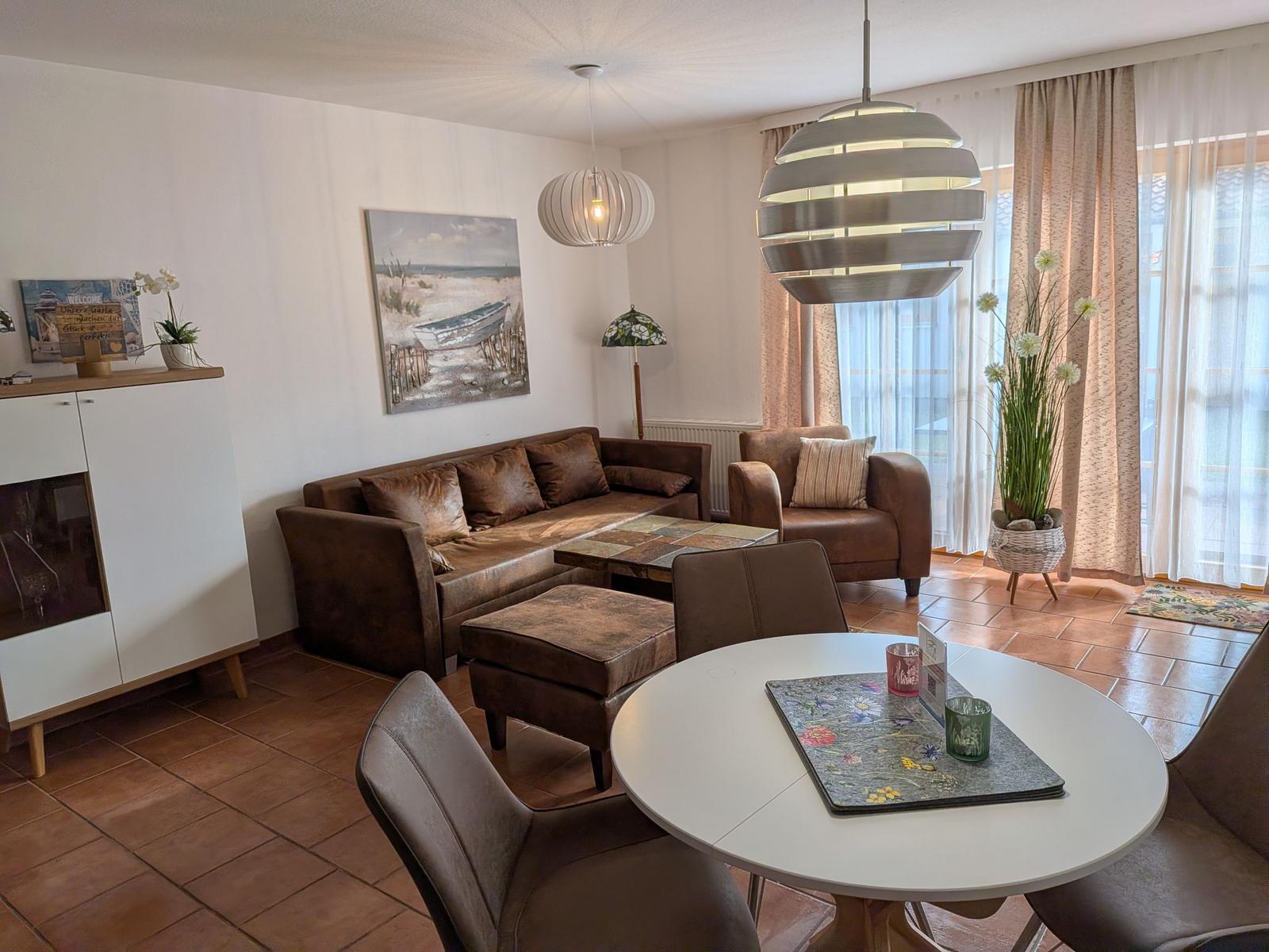 Wohnzimmer mit Sofa, Esstisch und Fenster mit Vorhängen.