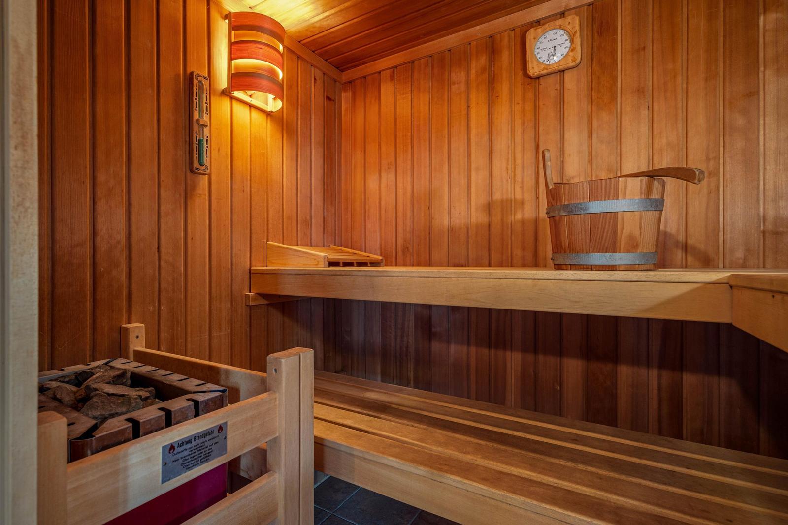 Sauna mit Holzbank, Holzregal und Holzbehälter mit Deckel.