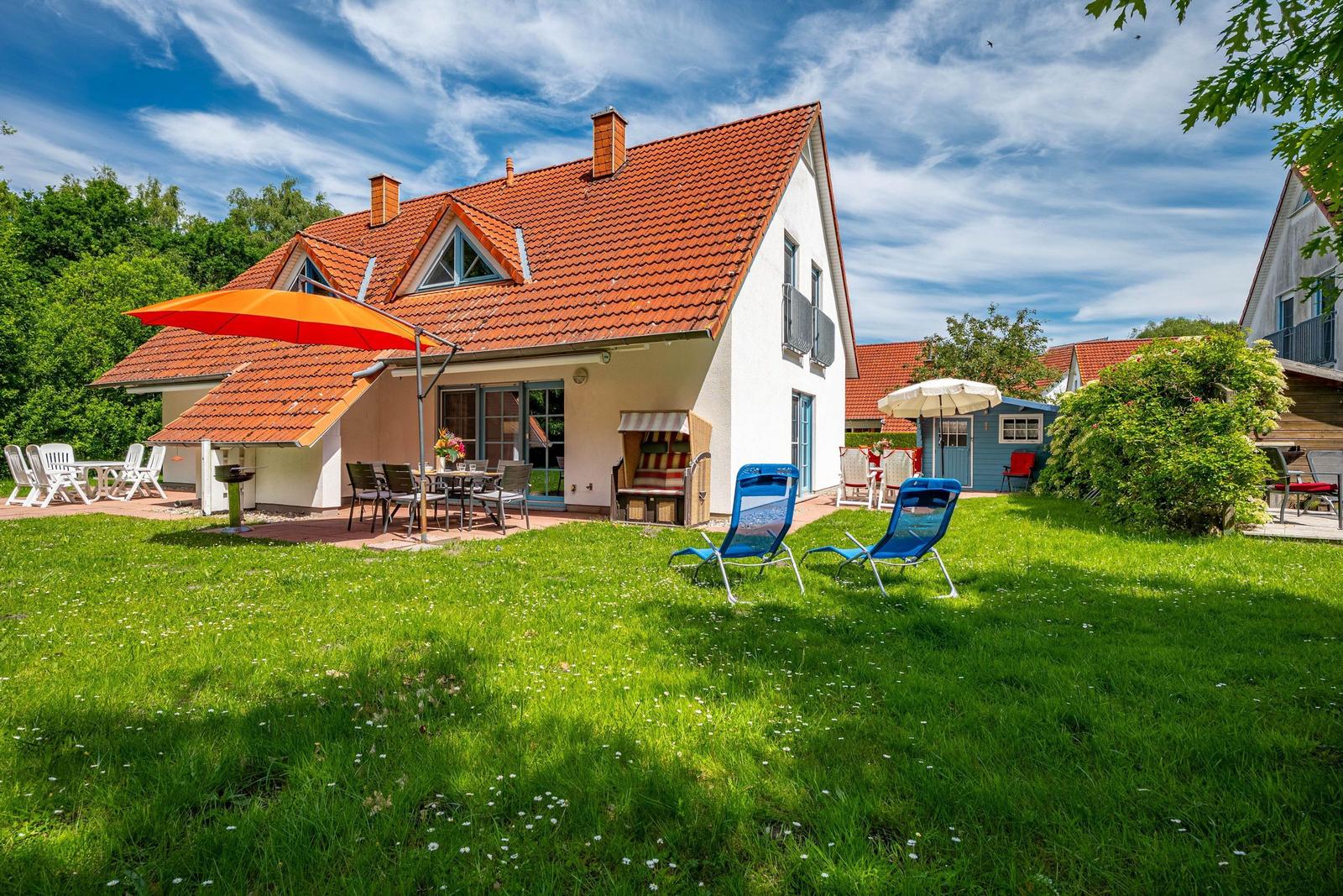 Haus mit Terrasse, Garten und Liegestühlen unter orangefarbener Markise.