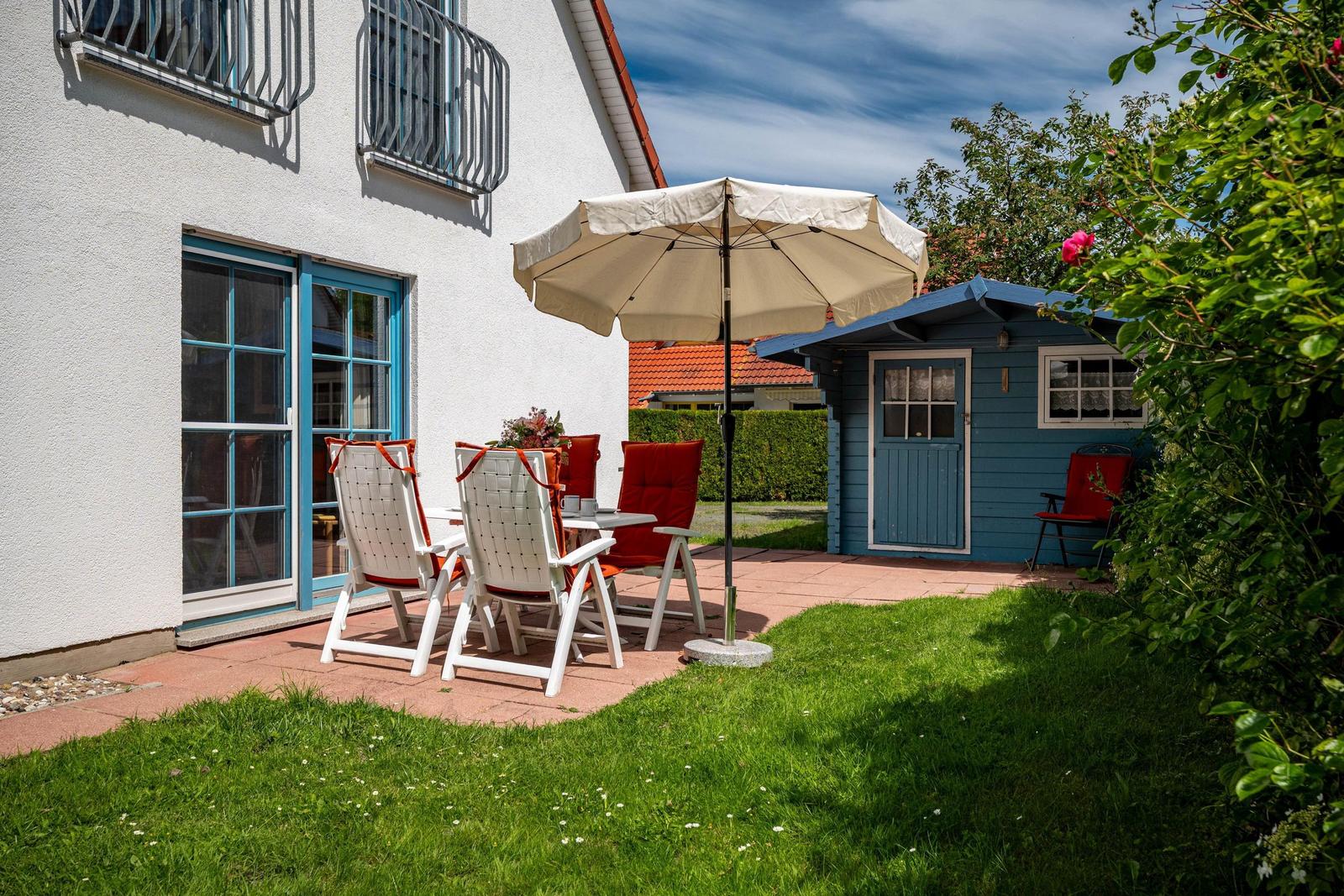 Terrasse mit Tisch, Stühlen und Sonnenschirm neben blauem Holzhaus.