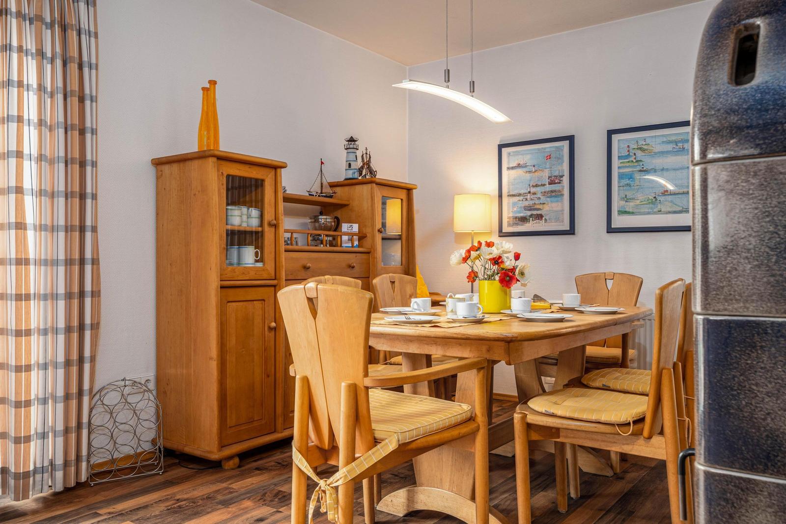 Esszimmer mit Holztisch, Stühlen und Küchenschränken. Wandbilder zeigen Hafenansichten.