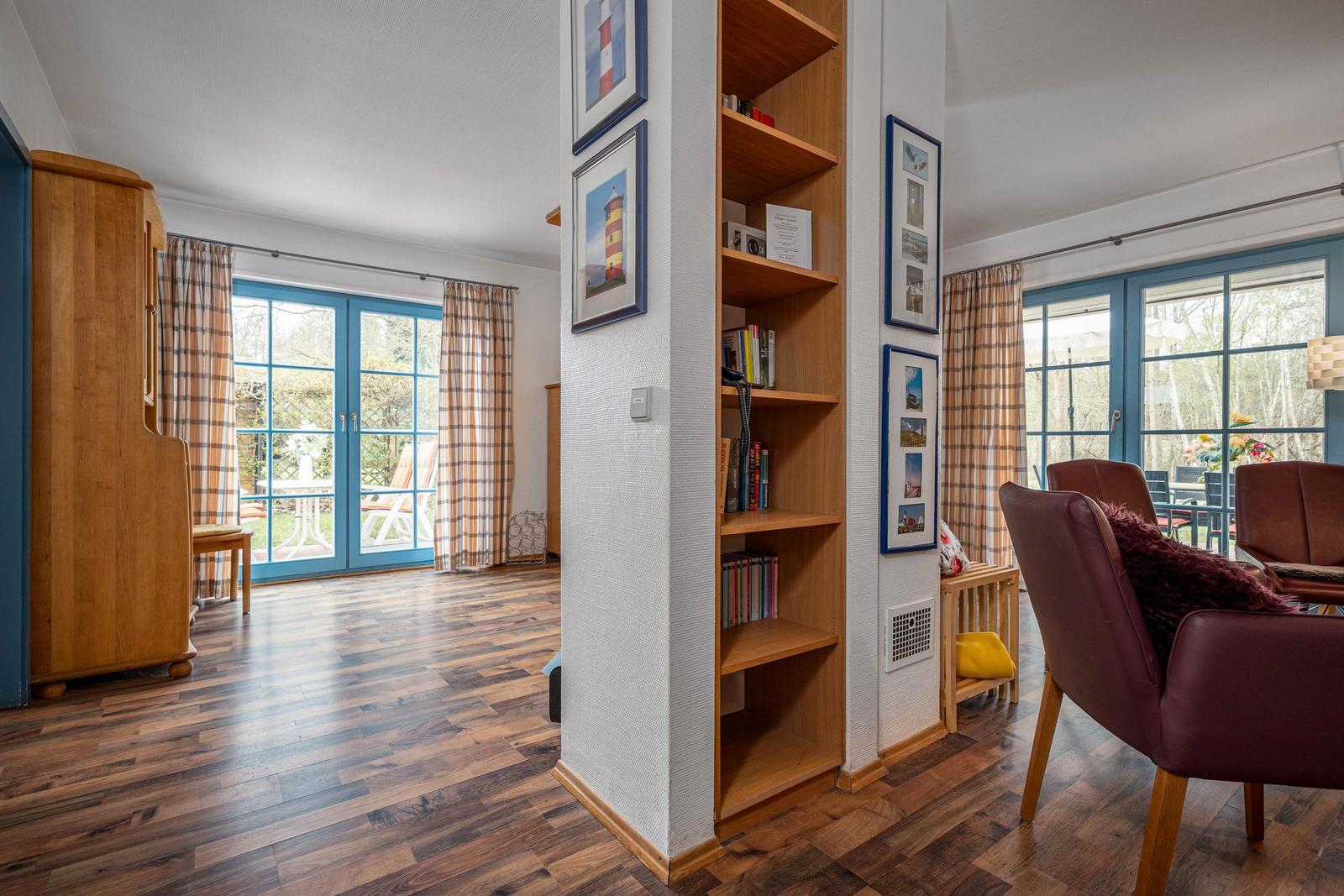 Wohnbereich mit Bücherregal, Sessel und Blick auf Balkon.