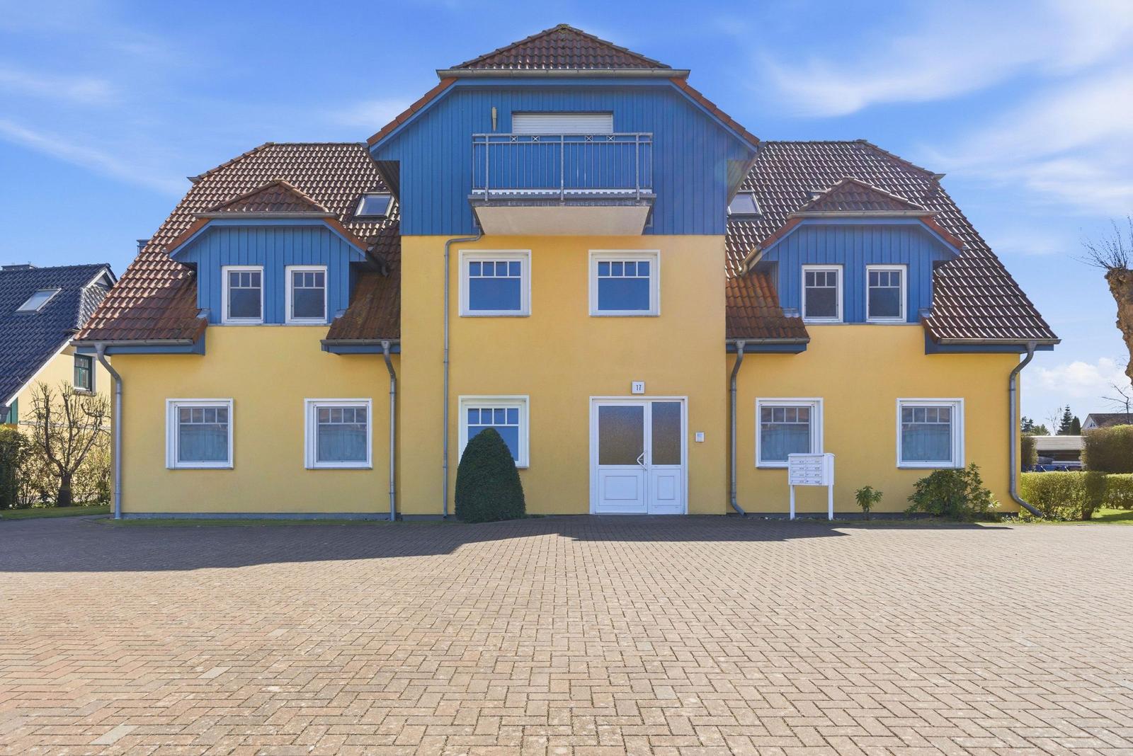 Ein zweistöckiges Haus mit gelbem und blauem Fassadenteil und rotem Dach. Vorderseite mit Eingangstür und Fenstern.