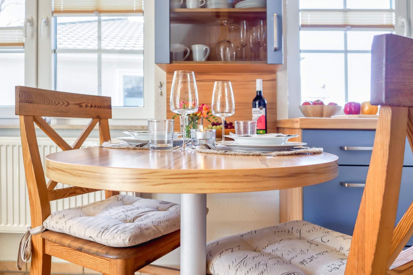 Rundes Esszimmer mit Holztisch, Stühlen und Geschirr. Hintergrund: Küchenmöbel und Fenster.